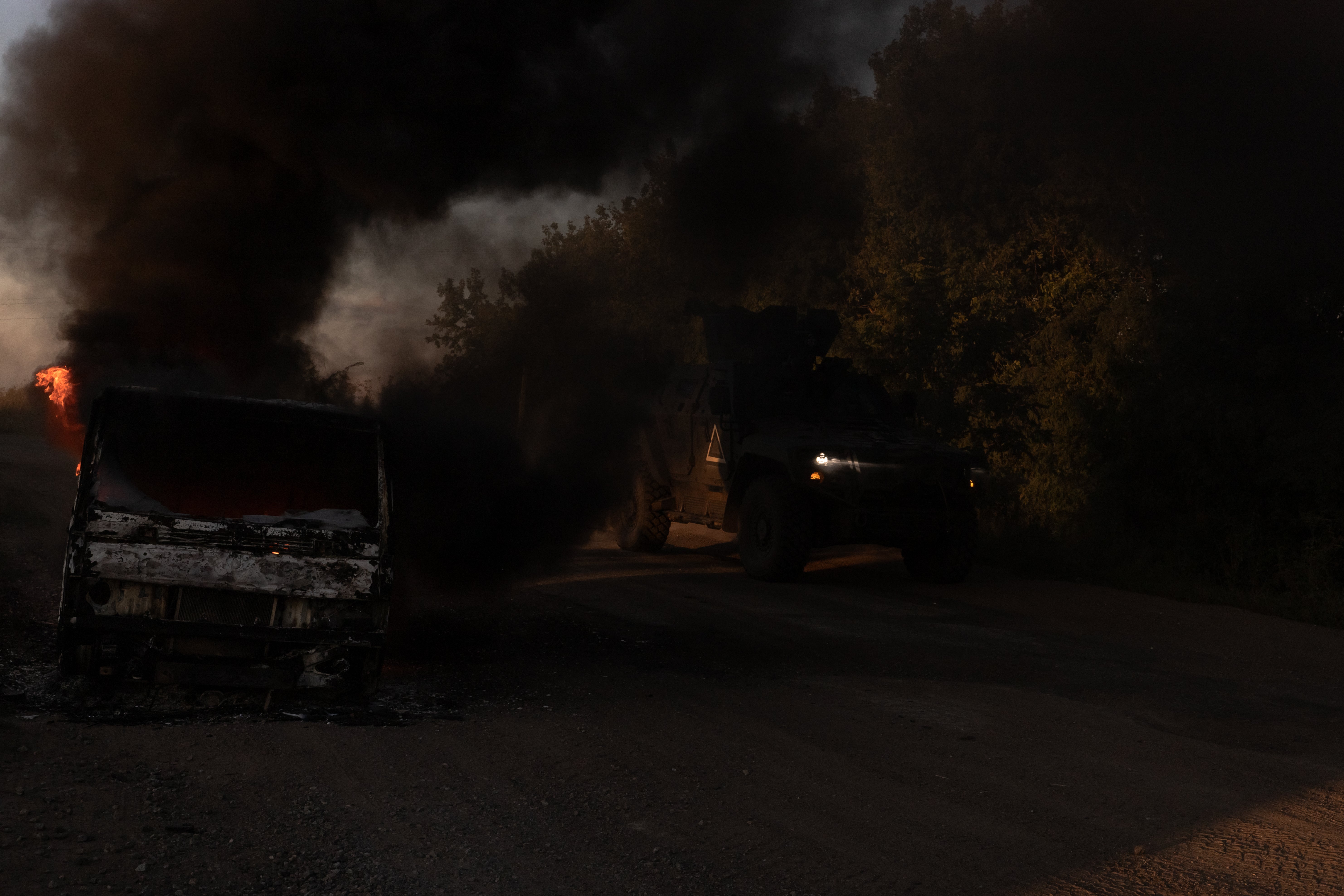 A Ukrainian armoured military vehicle drives past a burning car on a road near the border with Russia