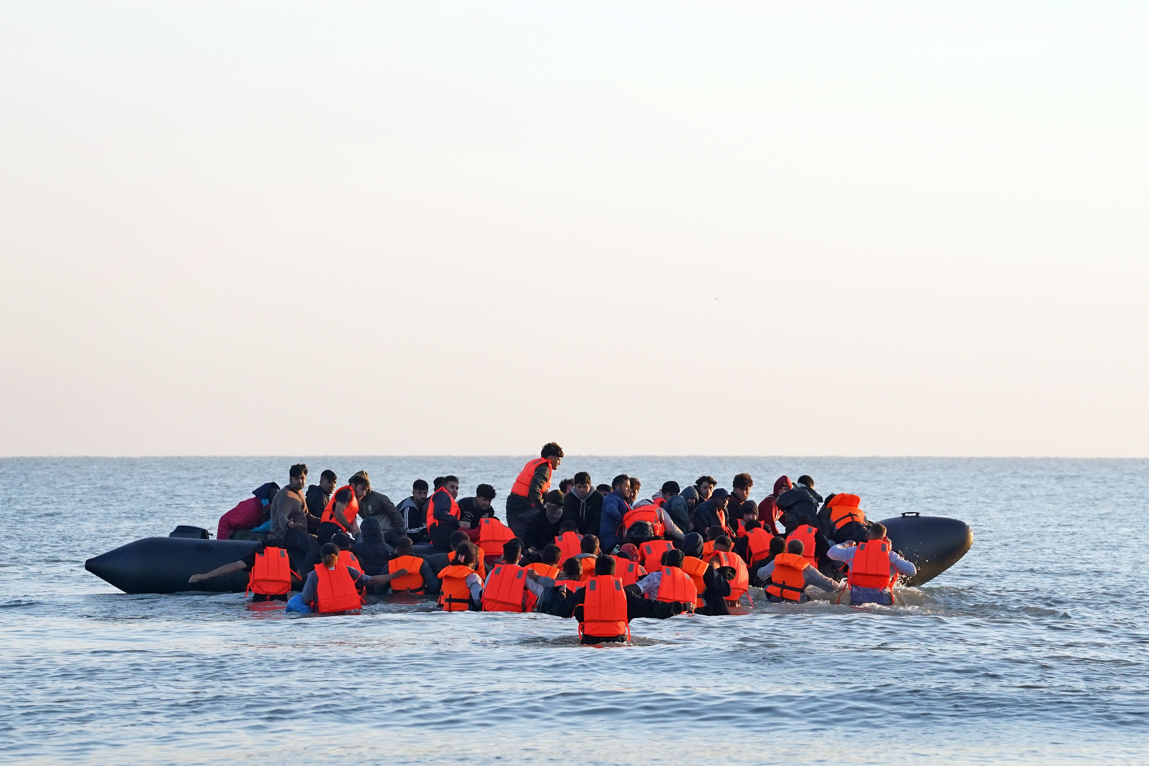 A group of people thought to be migrants wade through the sea to clamber aboard a small boat off the beach in Gravelines, France (PA)