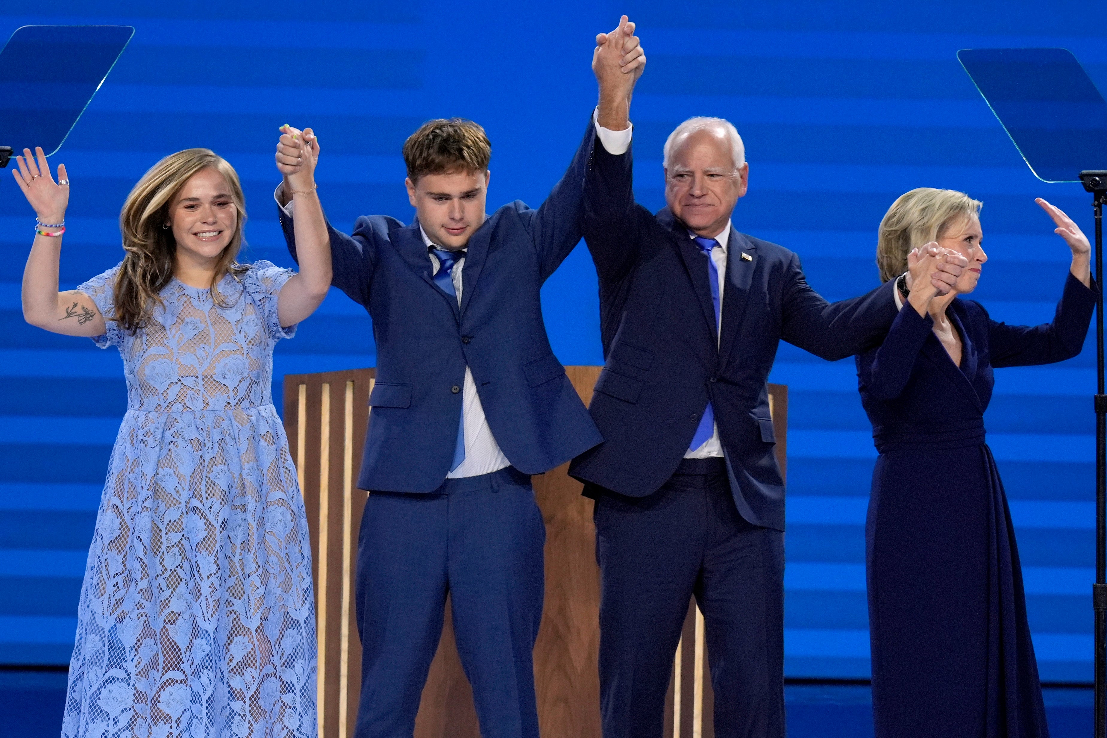 Hope, Gus, Tim and Gwen Walz (left to right) stand hand in hand on stage as the DNC crowd rows