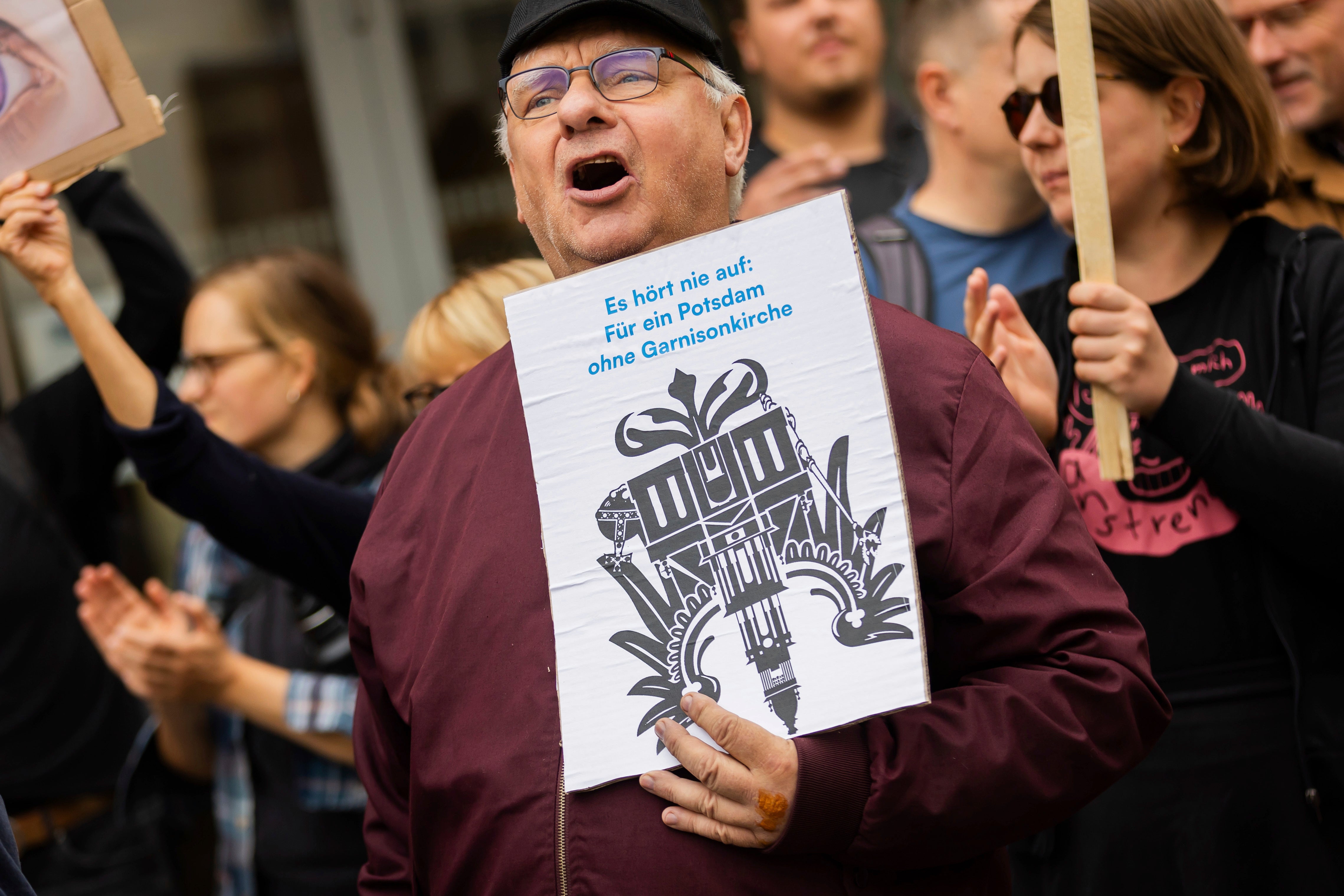 A participant in a protest organized by the ‘Citizens' Initiative for a Potsdam without a Garrison Church’ holds a sign showing the Garrison Church in the shape of an imperial eagle at the opening of the church's tower in Potsdam, Germany, Thursday Aug. 22, 2024. (Christoph Soeder/dpa via AP)