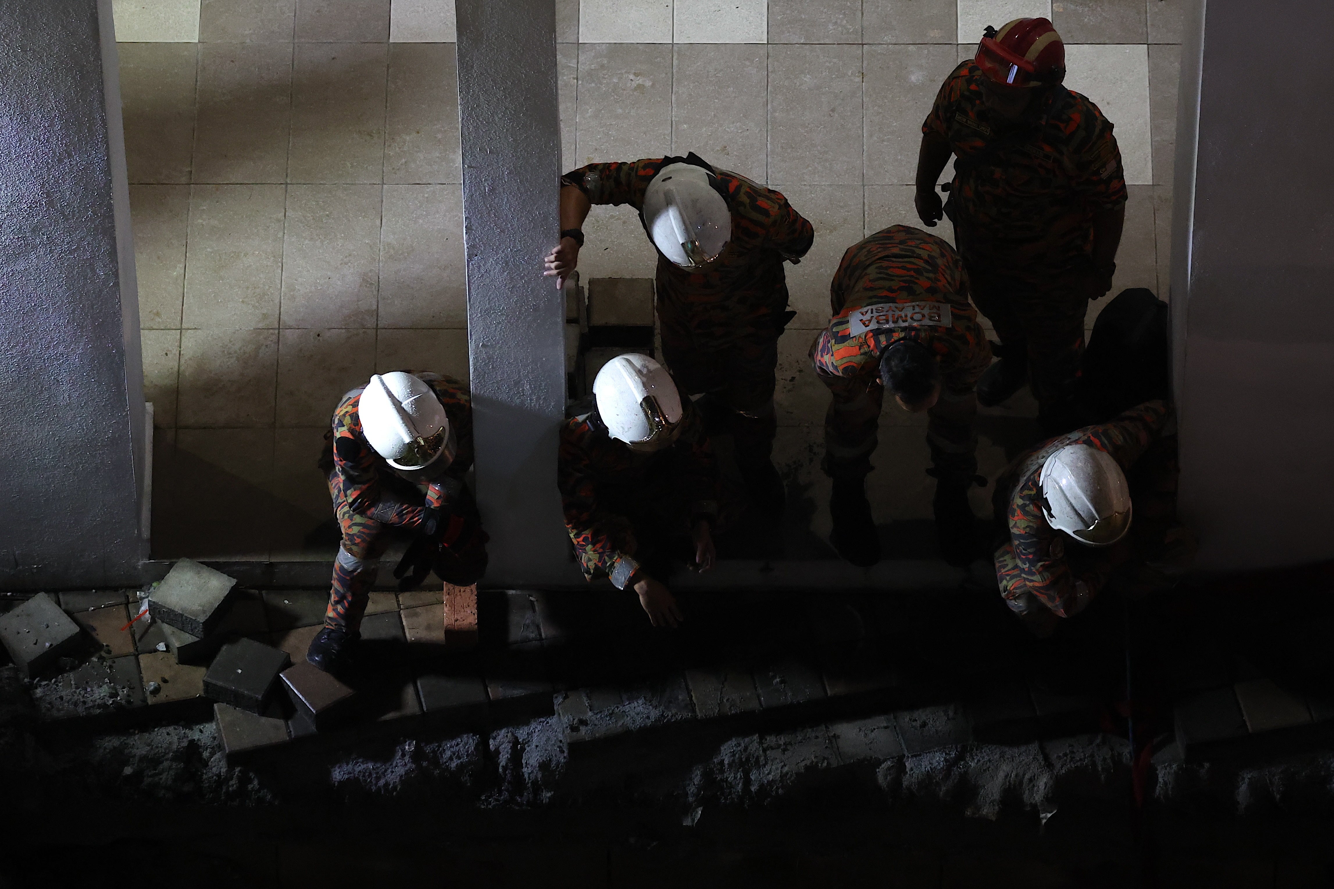 Malaysia Fire and Rescue Department officers inspect the site where a woman fell