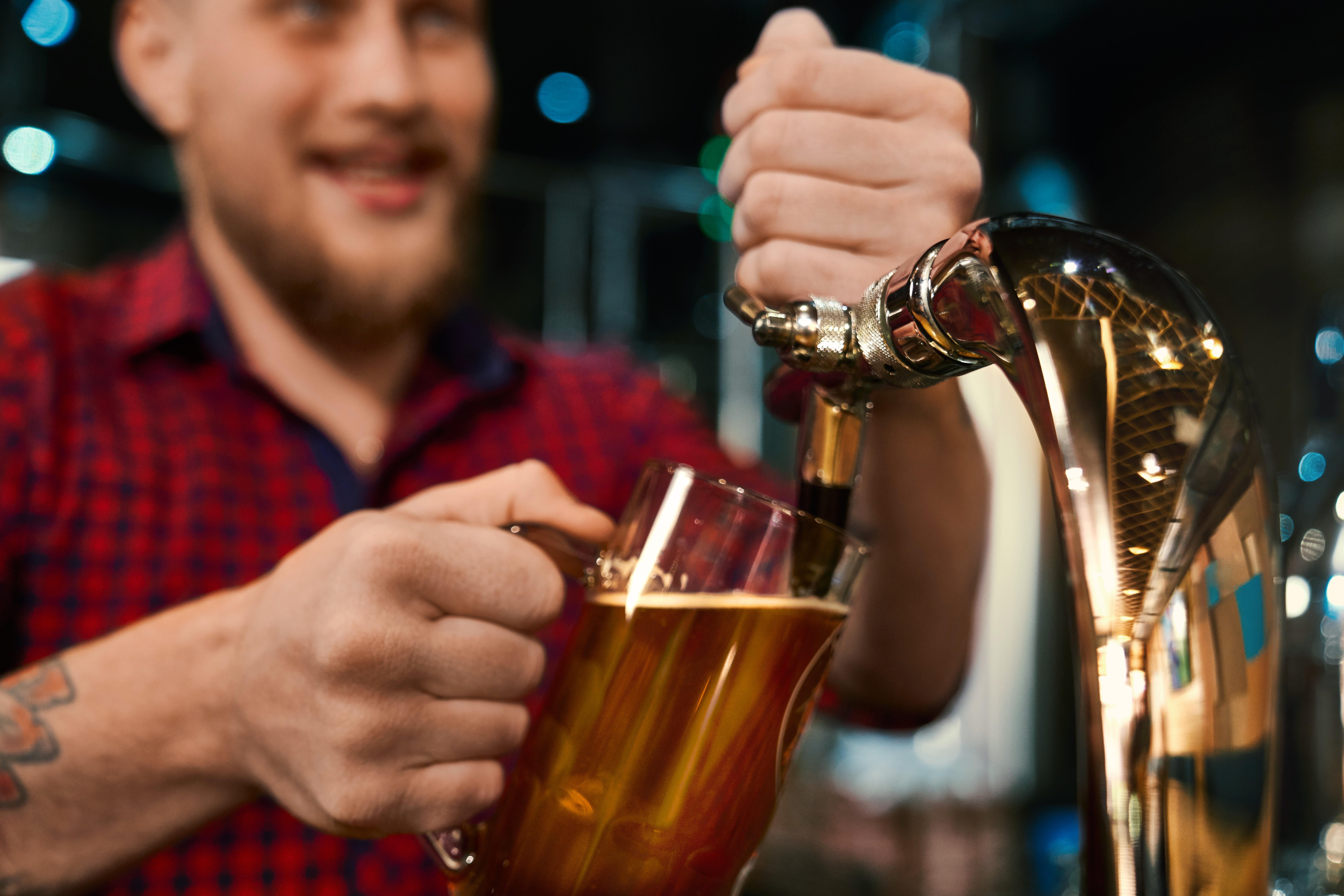 Man with a beard wearing a red shirt pulling a pint behind the bar