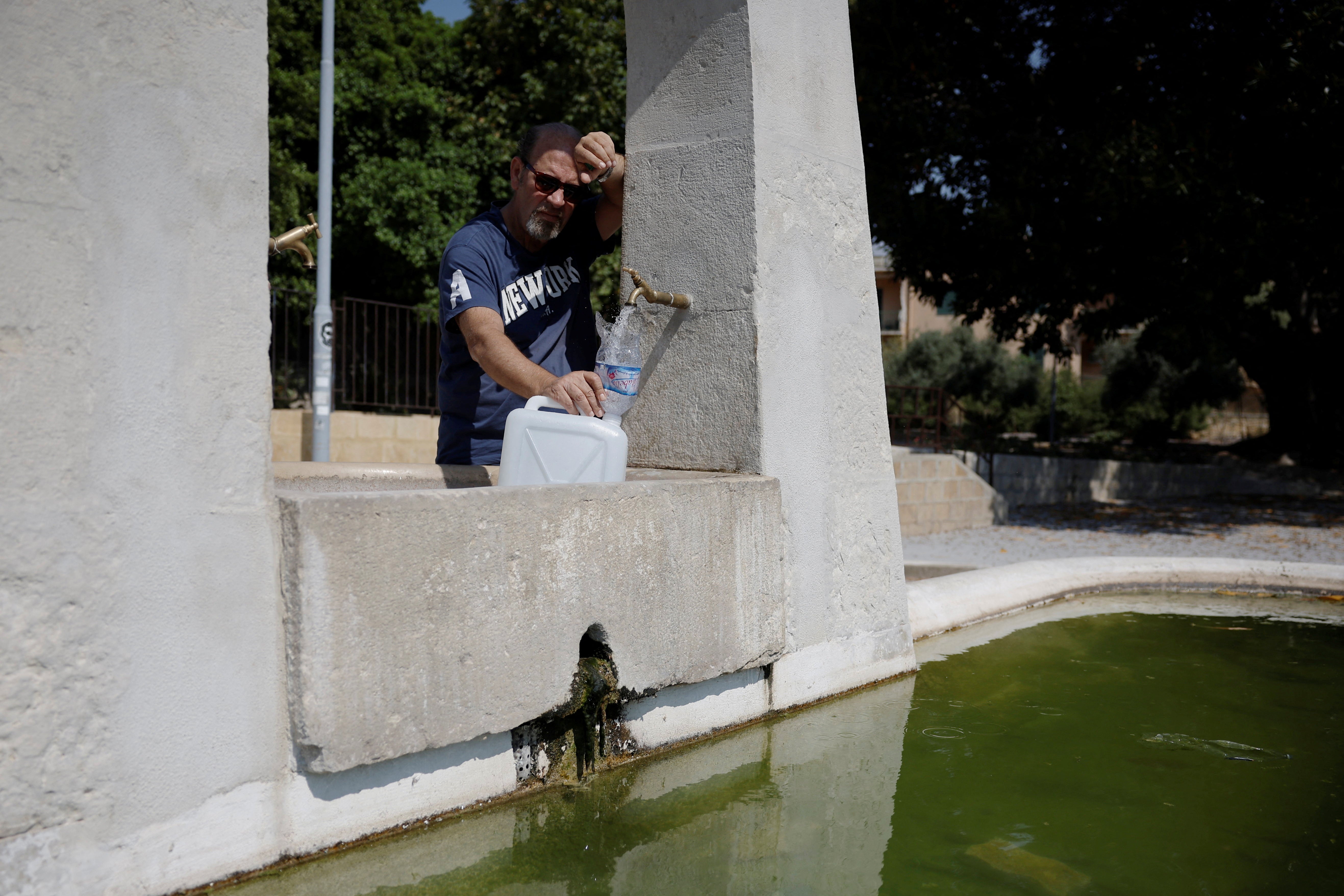 Salvatore Celauro fills a container with water at a fountain following a drought on the Italian island of Sicily, in Agrigento, Italy, August 25