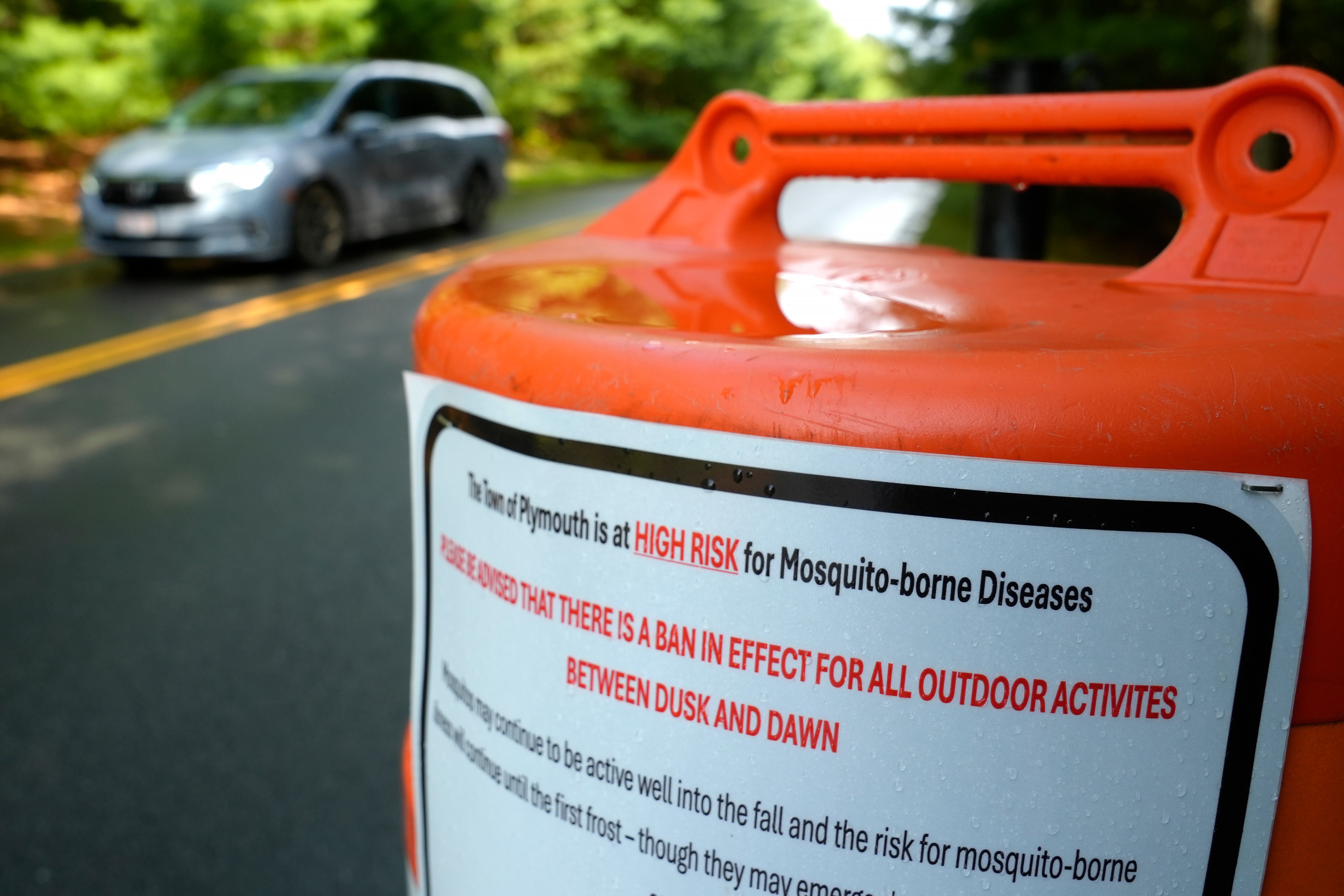 A vehicle passes a sign warning people that the town of Plymouth is at ‘high risk’ for mosquito-borne diseases. Parks and fields in the community have been closed for certain hours to reduce that risk.