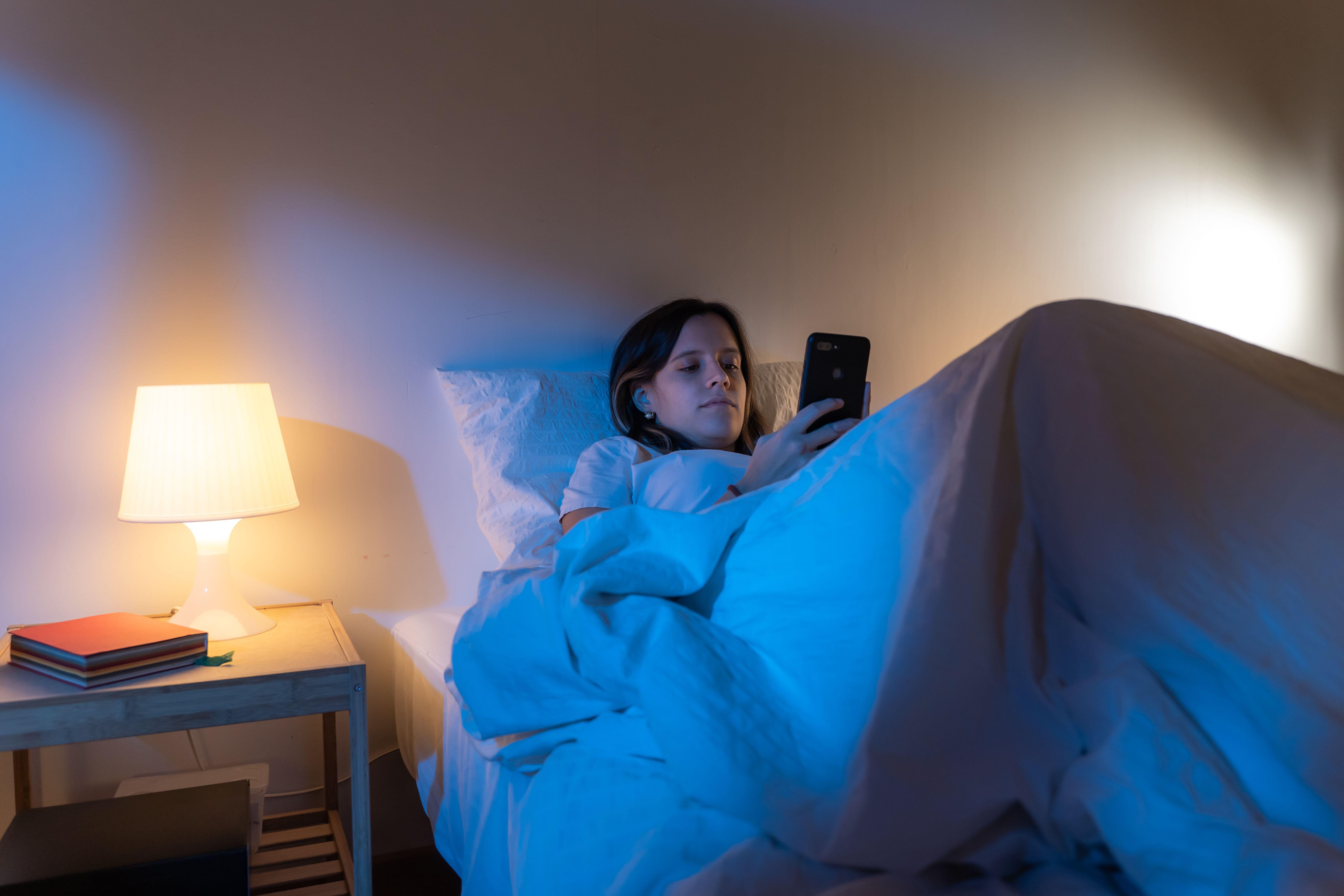 Girl looking her smart phone doom scrolling on bed in the middle of the night (Alamy/PA)