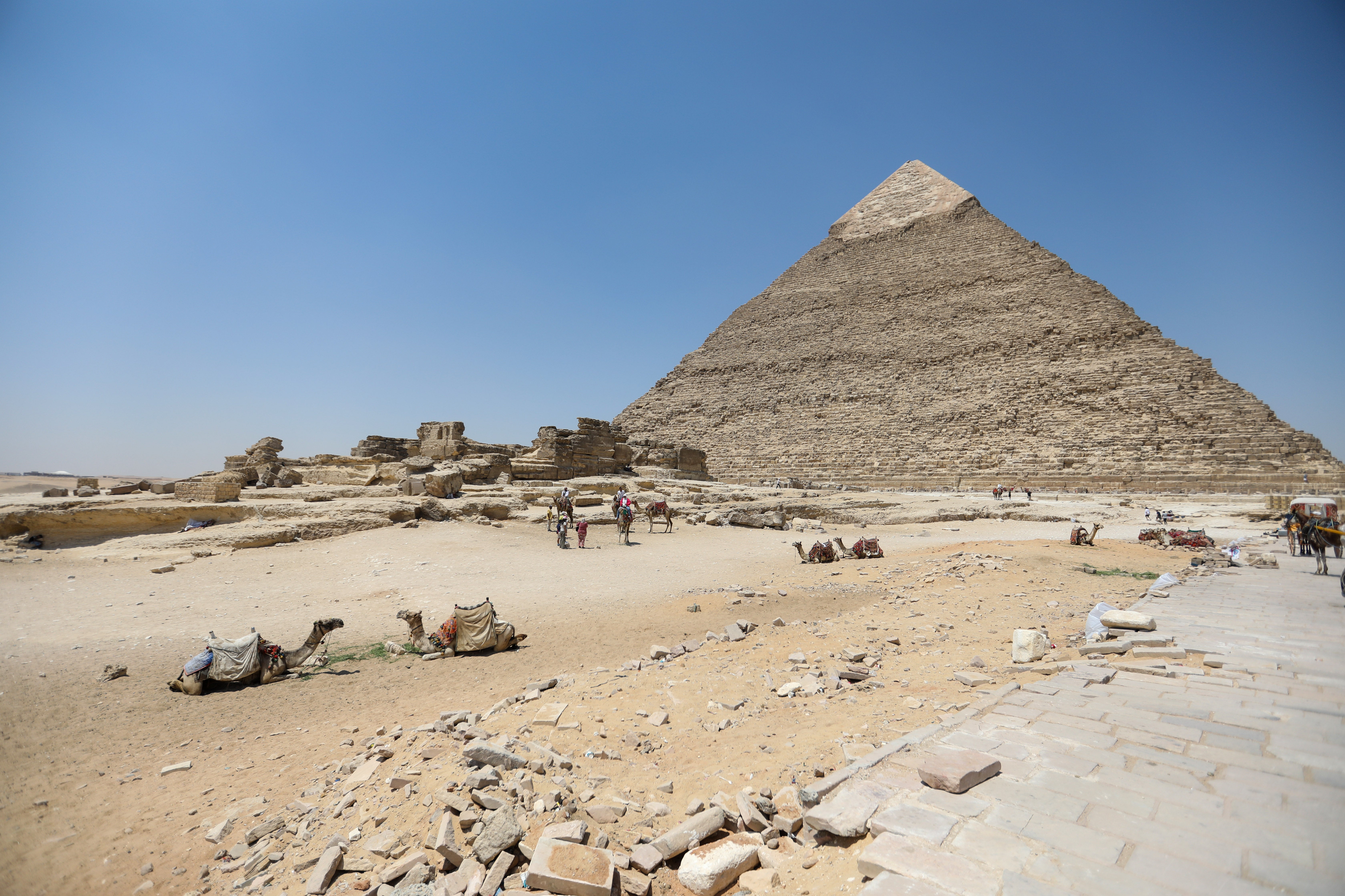 Tourists walk past pyramids of Khufu, Khafre, and Menkaure in Giza