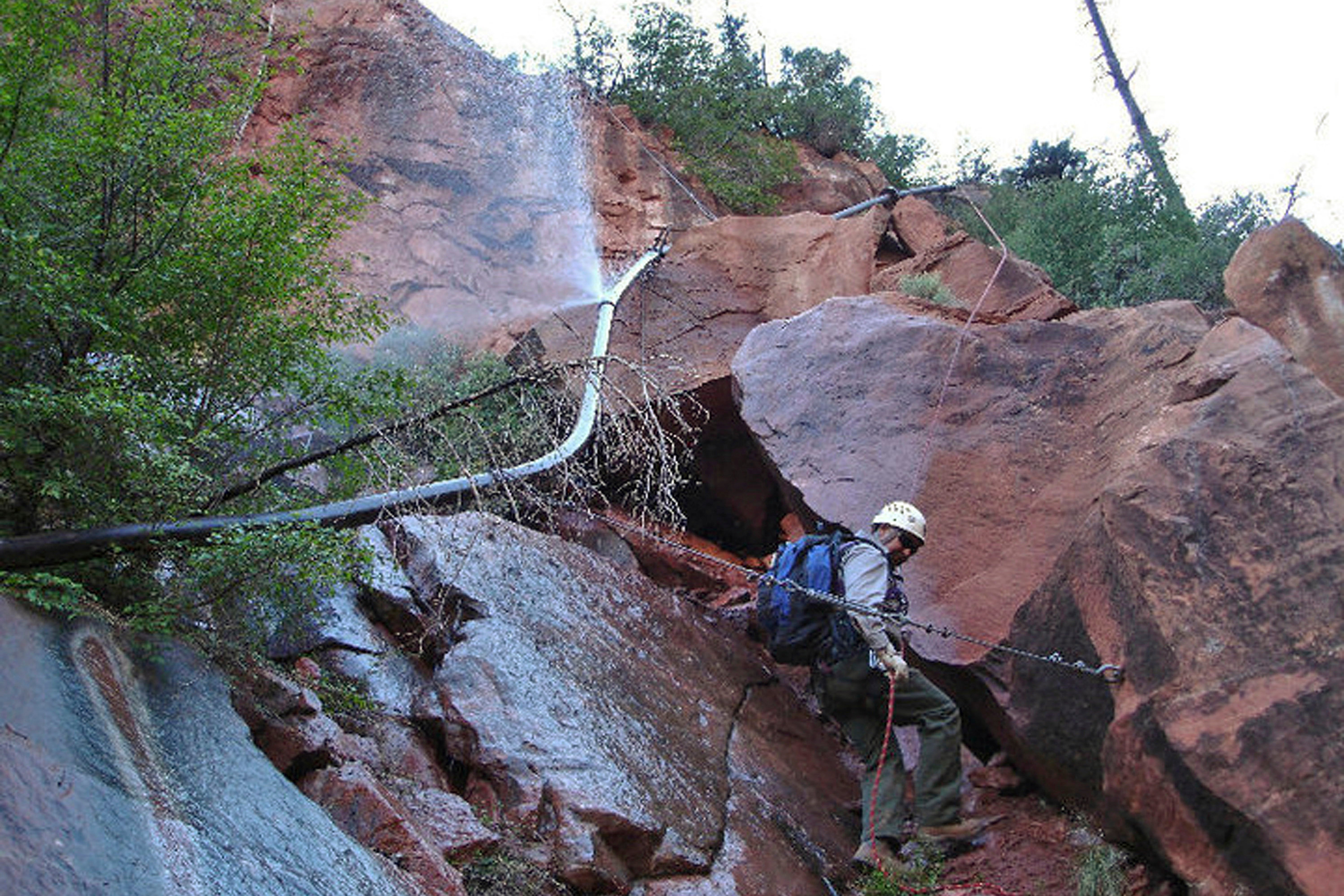 Water spraying from a break in an exposed section of the Grand Canyon trans-canyon waterline as a worker attempts repairs