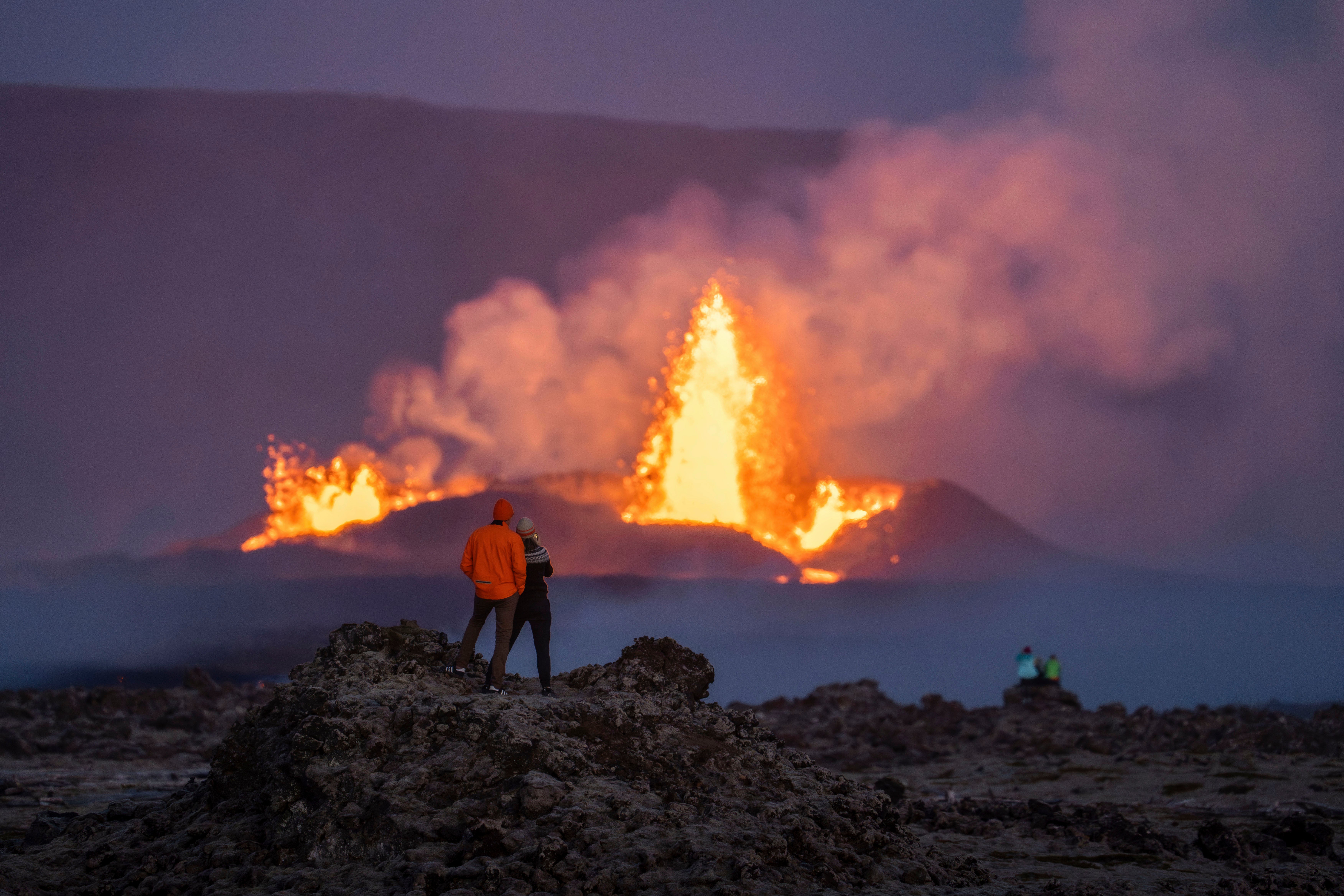 People watch the erupting craters and the lava fountains from the old lava fields around the eruption site on the Reykjanes Peninsula, in Iceland, Wednesday, Aug. 28, 2024. (AP Photo/Marco di Marco)