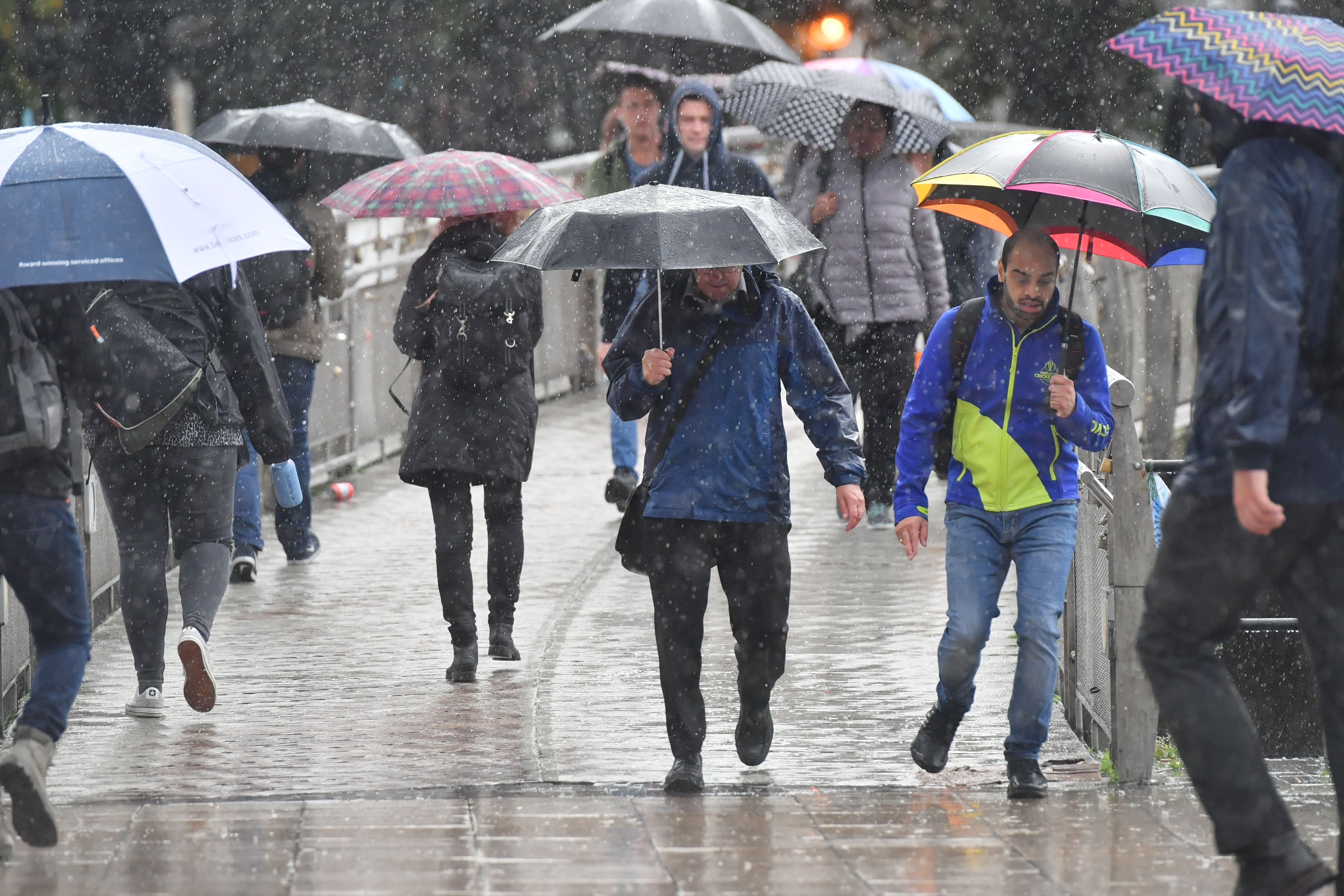 People with umbrellas walk in the street (Ben Birchall/PA)