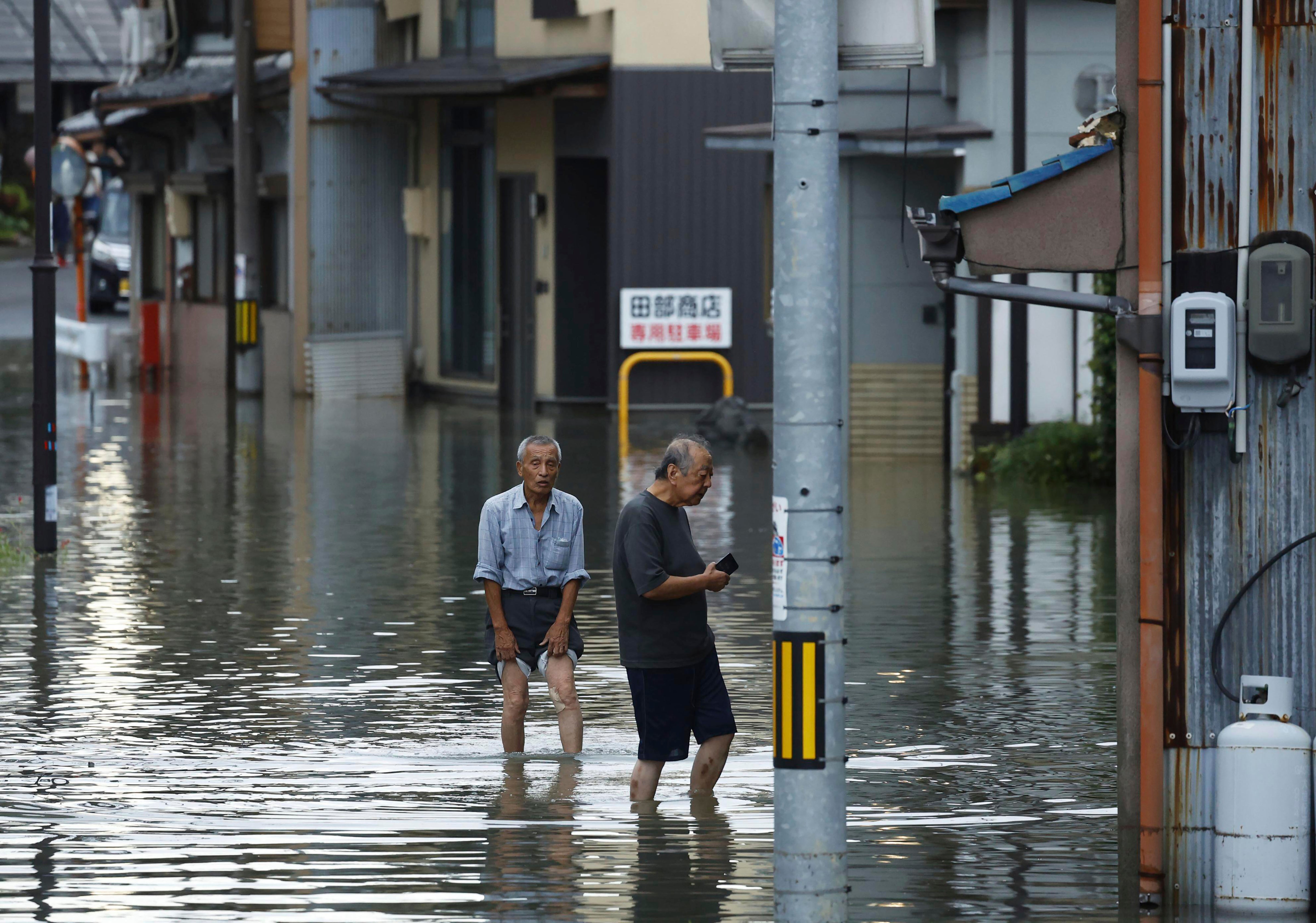 People wade through a flooded street as the city was hit by heavy rain in Ogaki, central Japan