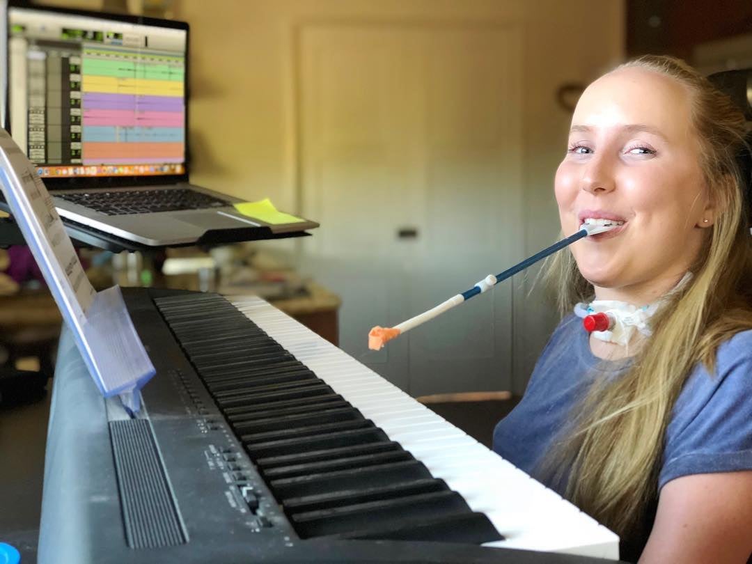 Grace Fisher playing the piano with a stick in her mouth