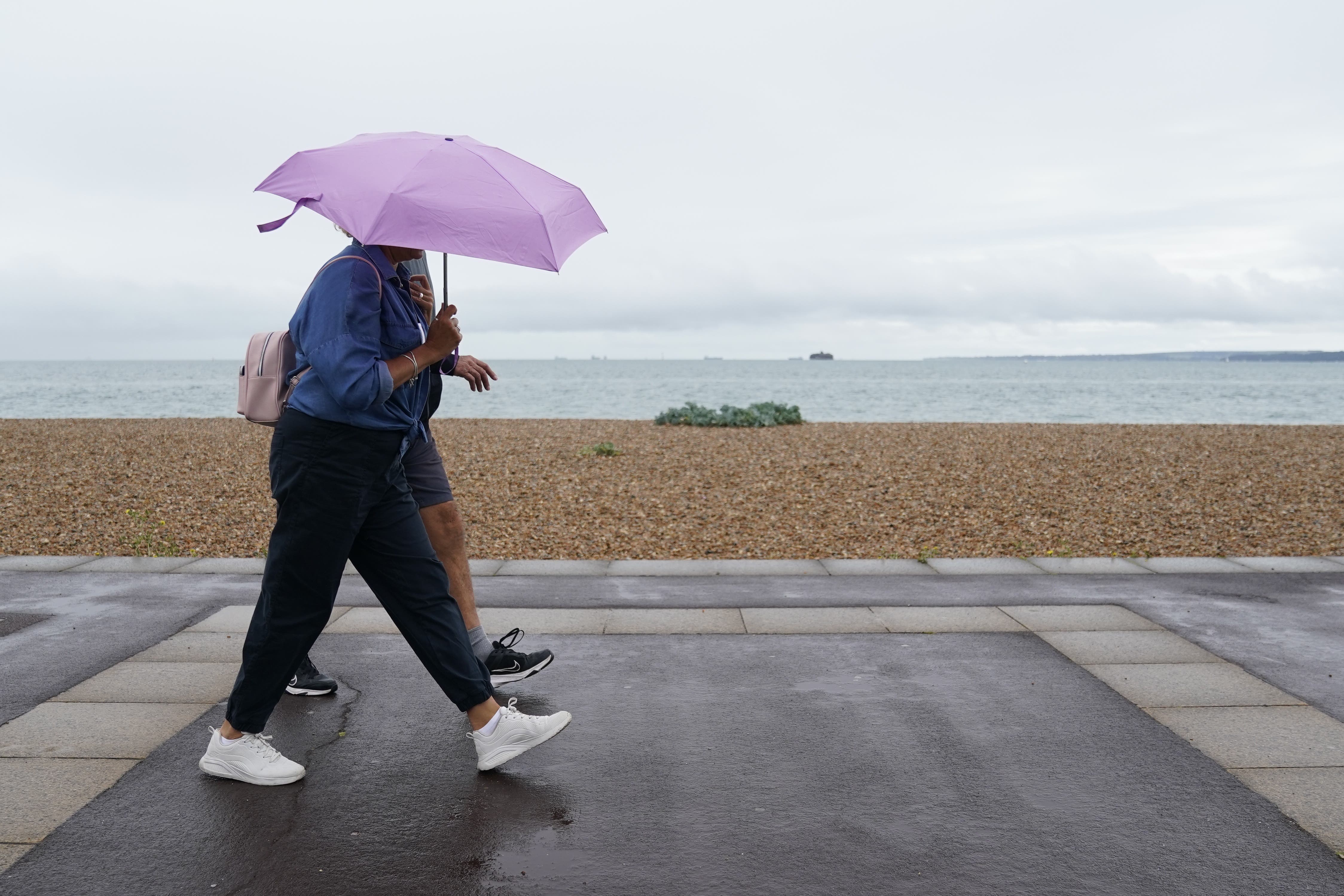 People shelter from the rain under umbrellas as walk along Southsea Beach in Hampshire (PA)