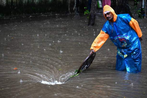 File: A municipal worker standing near a manhole in a flooded street in India