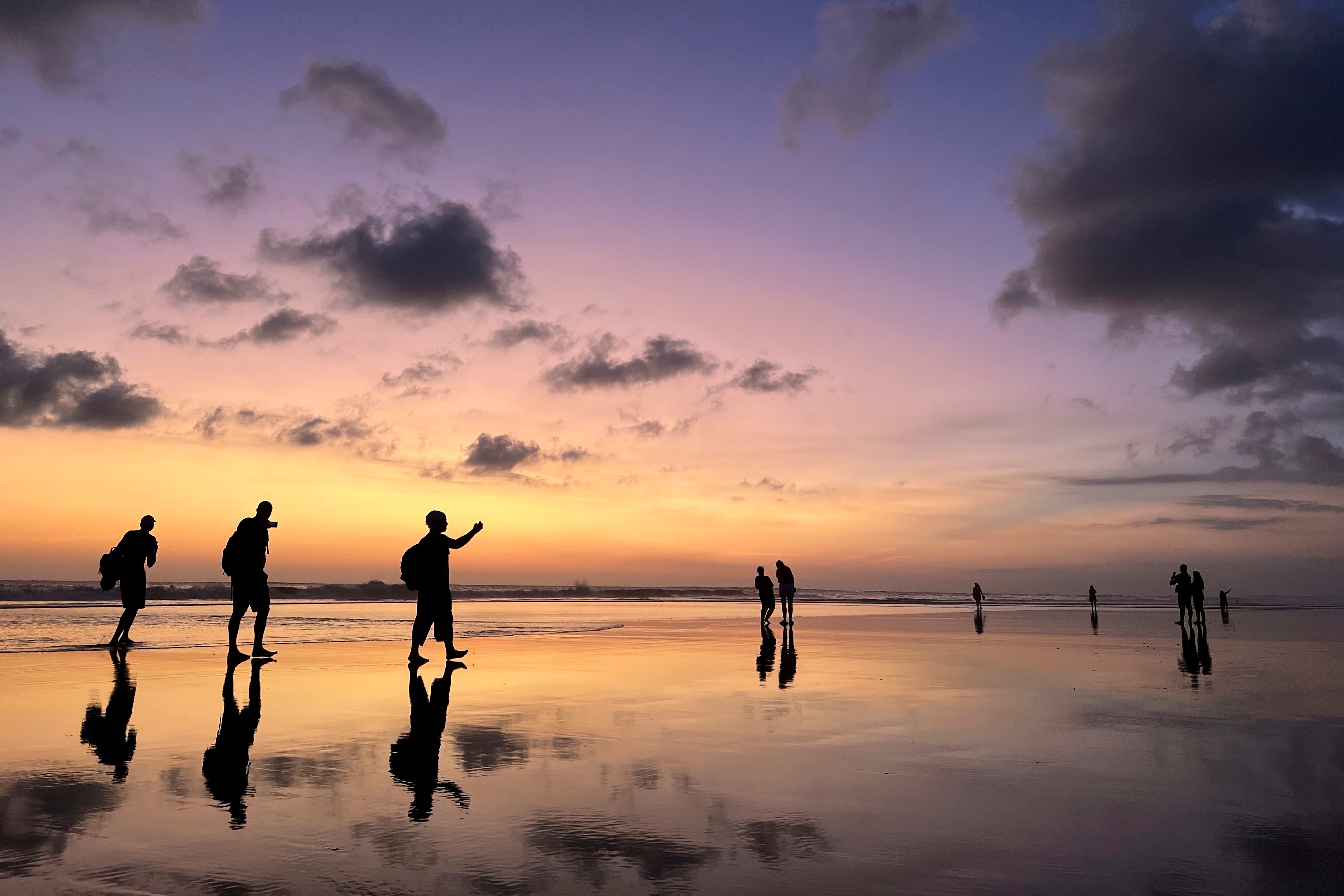 Tourists laugh and take selfies at sunset on Seminyak Beach in Bali