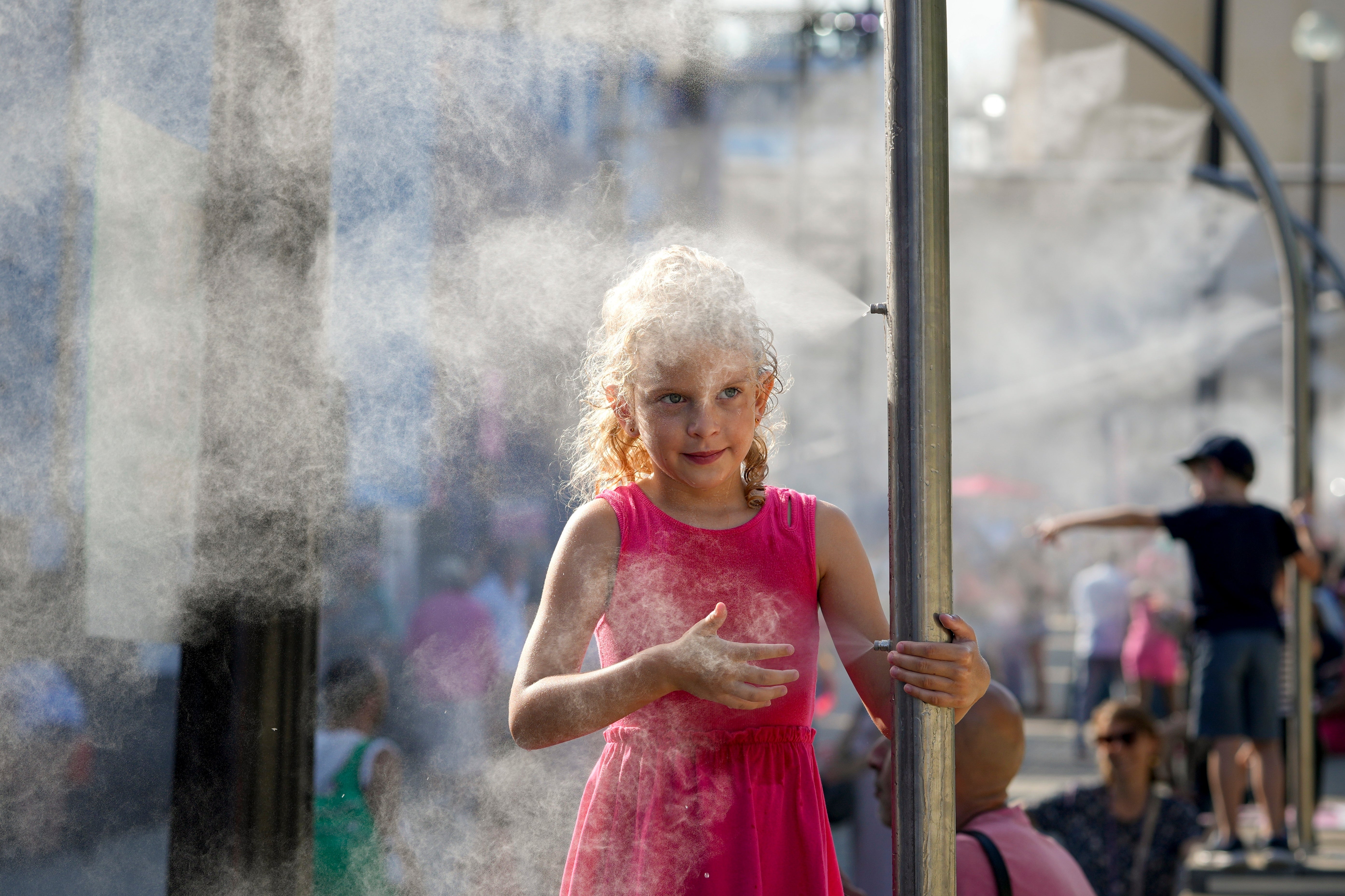 Anna, 7, cools off under a misting fountain on a hot afternoon during the 2024 Summer Olympics,