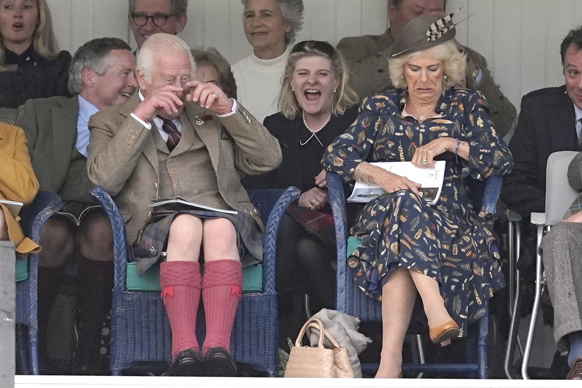 King Charles, wiping his eyes with laughter, and Camilla watching the Highland Games