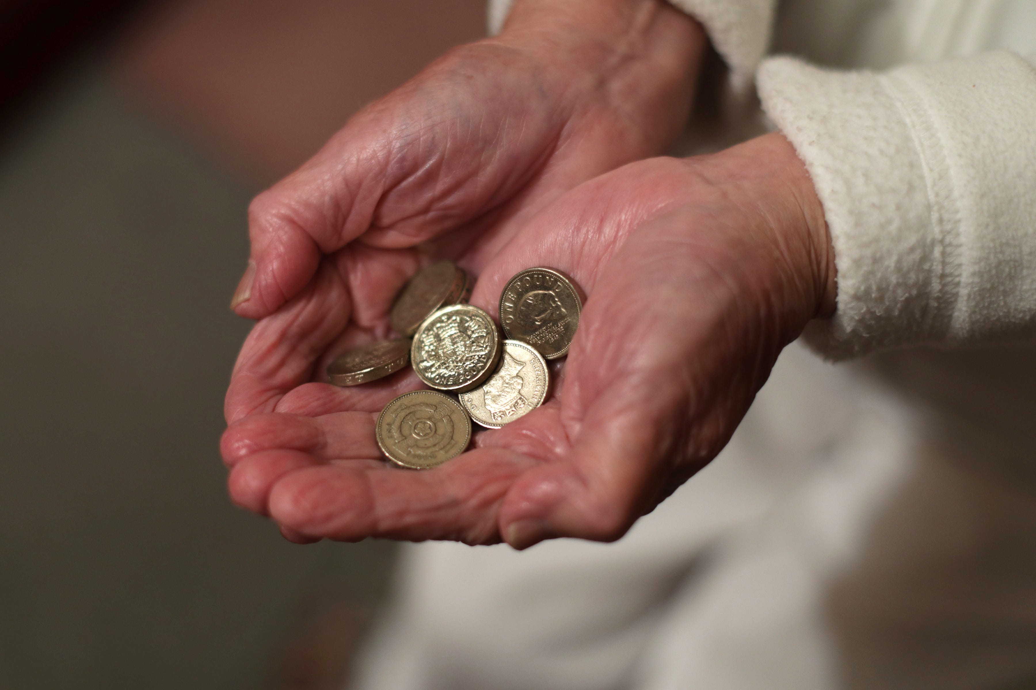An elderly woman holding pound coins in her hands (PA)