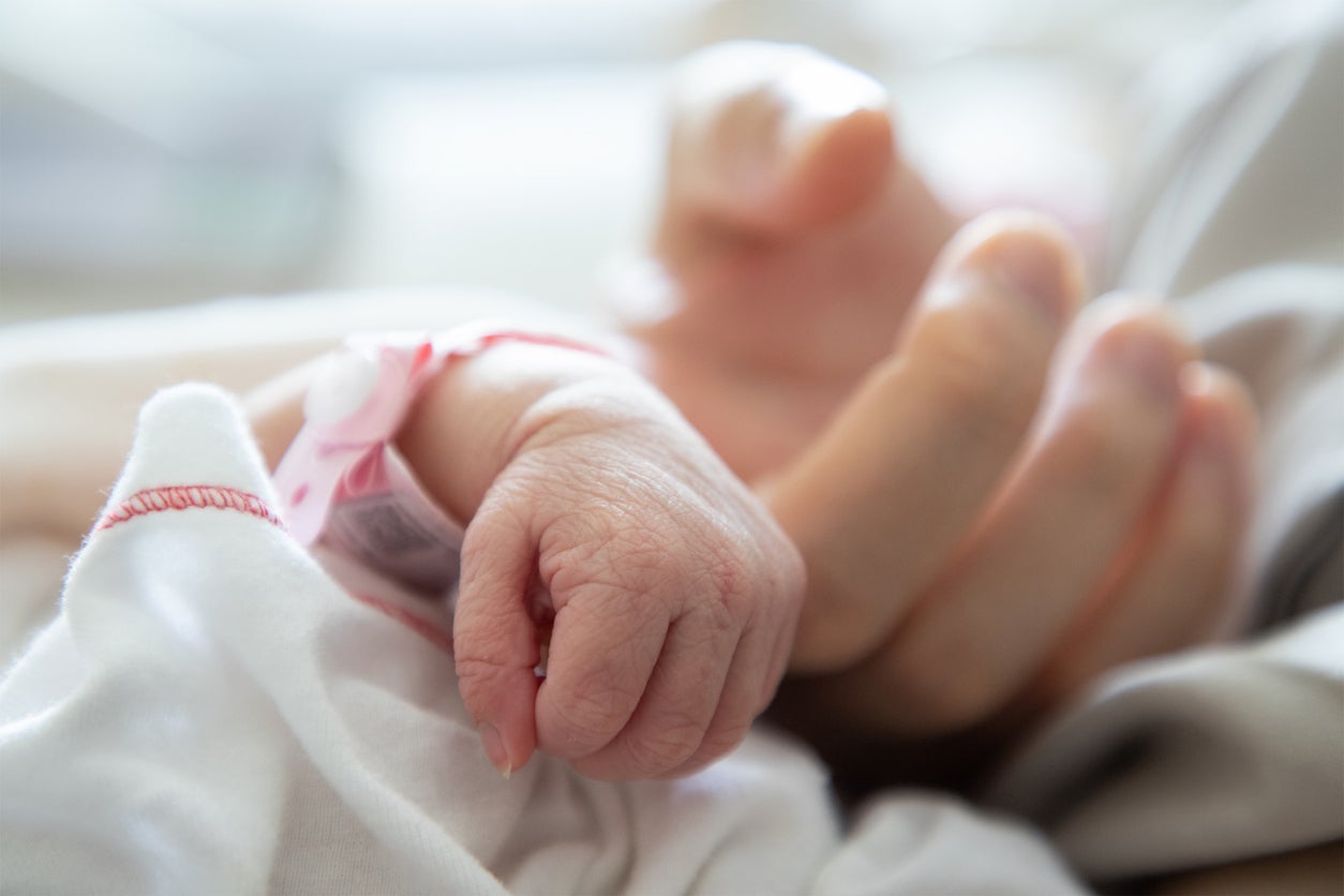 A newborn baby holds its mother’s finger in a hospital bed. Babies at high risk of SIDS may not be metabolizing glucose and fats in the same way at birth as those lower at risk.