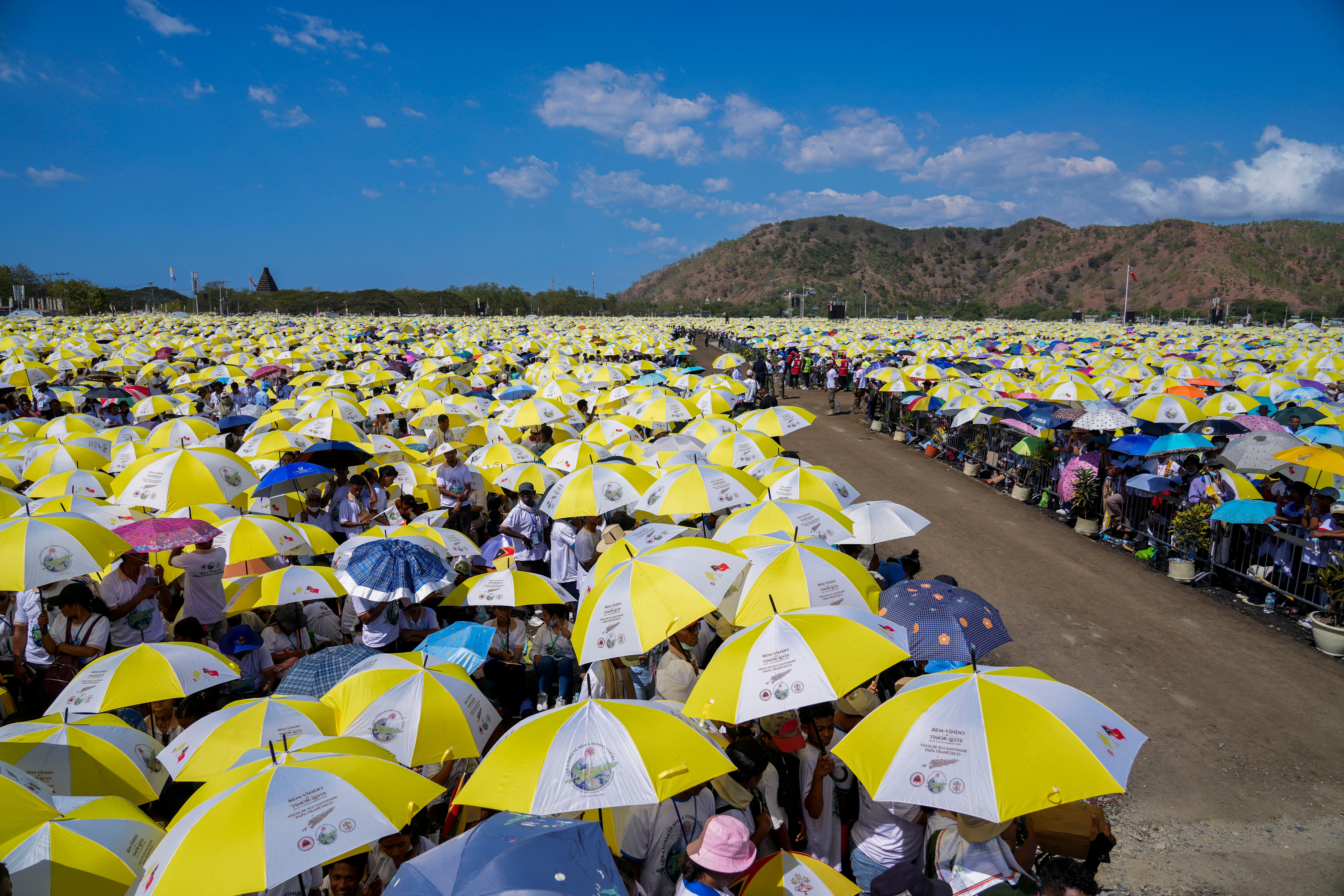 Faithful use umbrellas with the colors of the Vatican flag to shield themselves from the sun