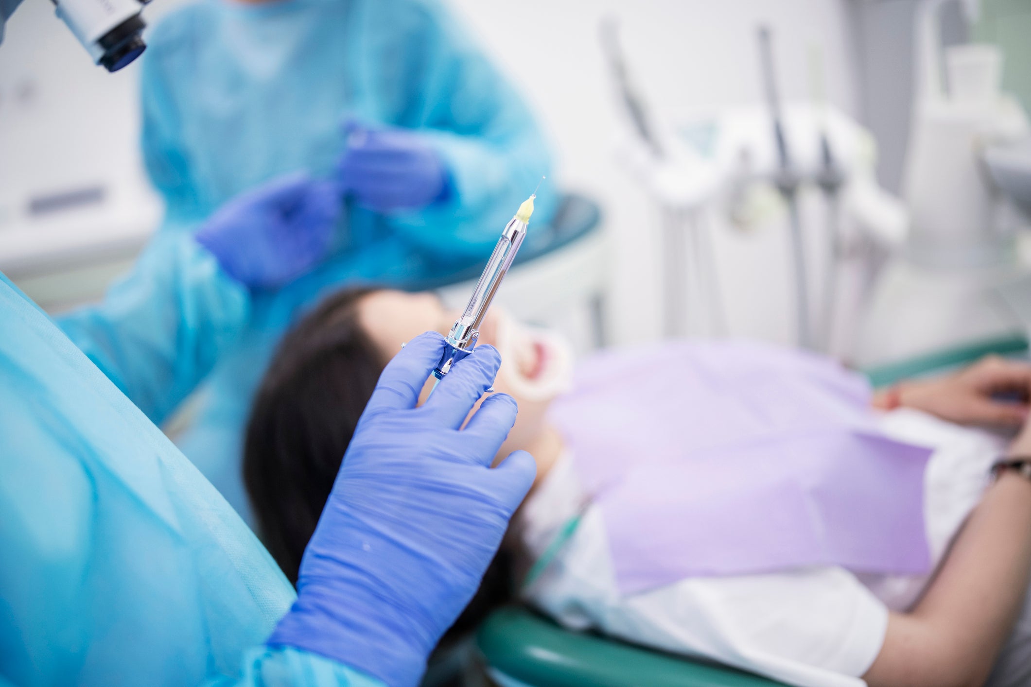 File: Unrecognizable person giving anaesthesia to the female patient laying on dentist chair, preparation for surgery.