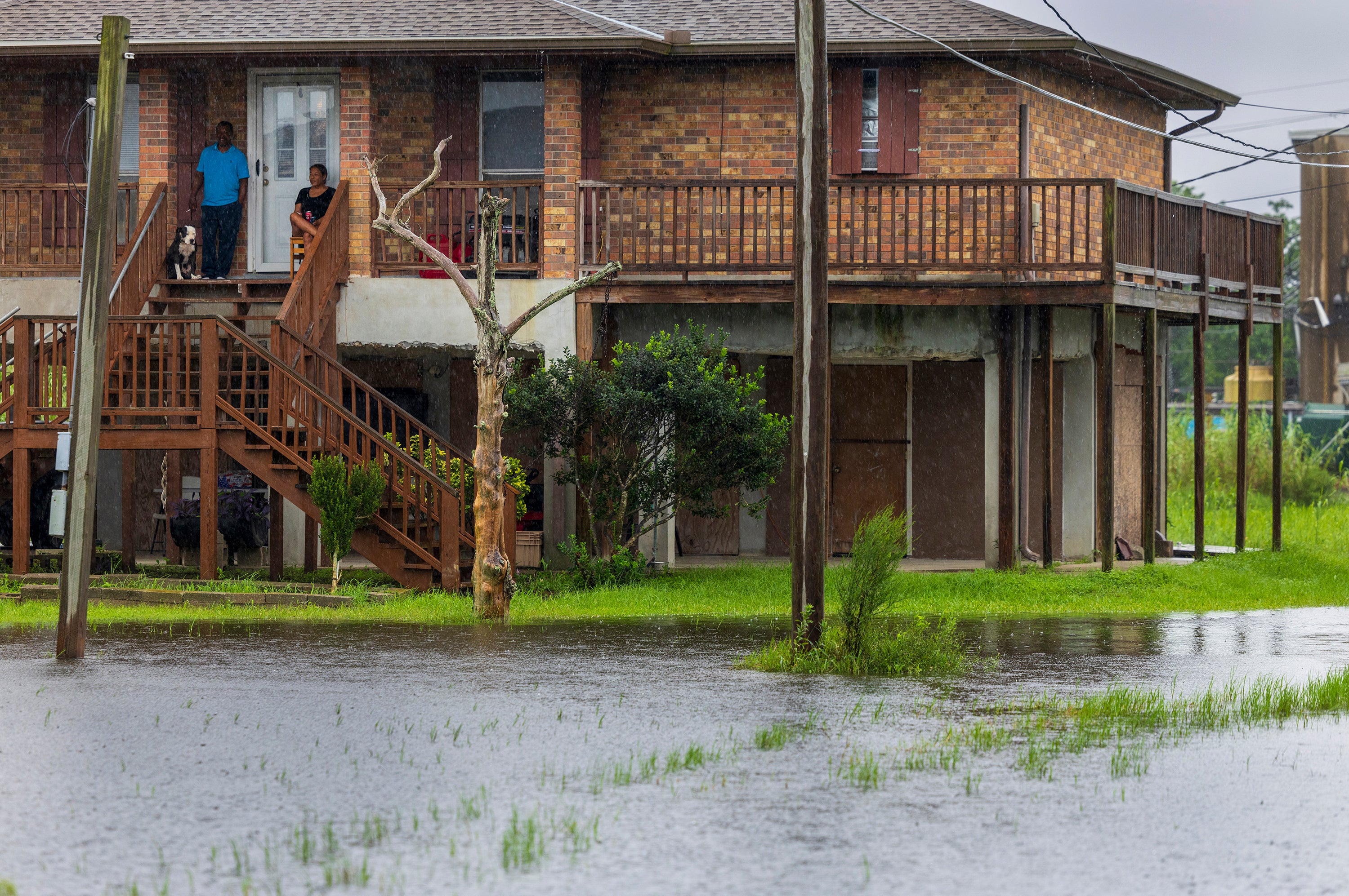 Dulac residents, top left, sit on their front porch and watch water rise around their elevated home on Wednesday. Dulac is already experiencing storm surge and flooding from Francine.