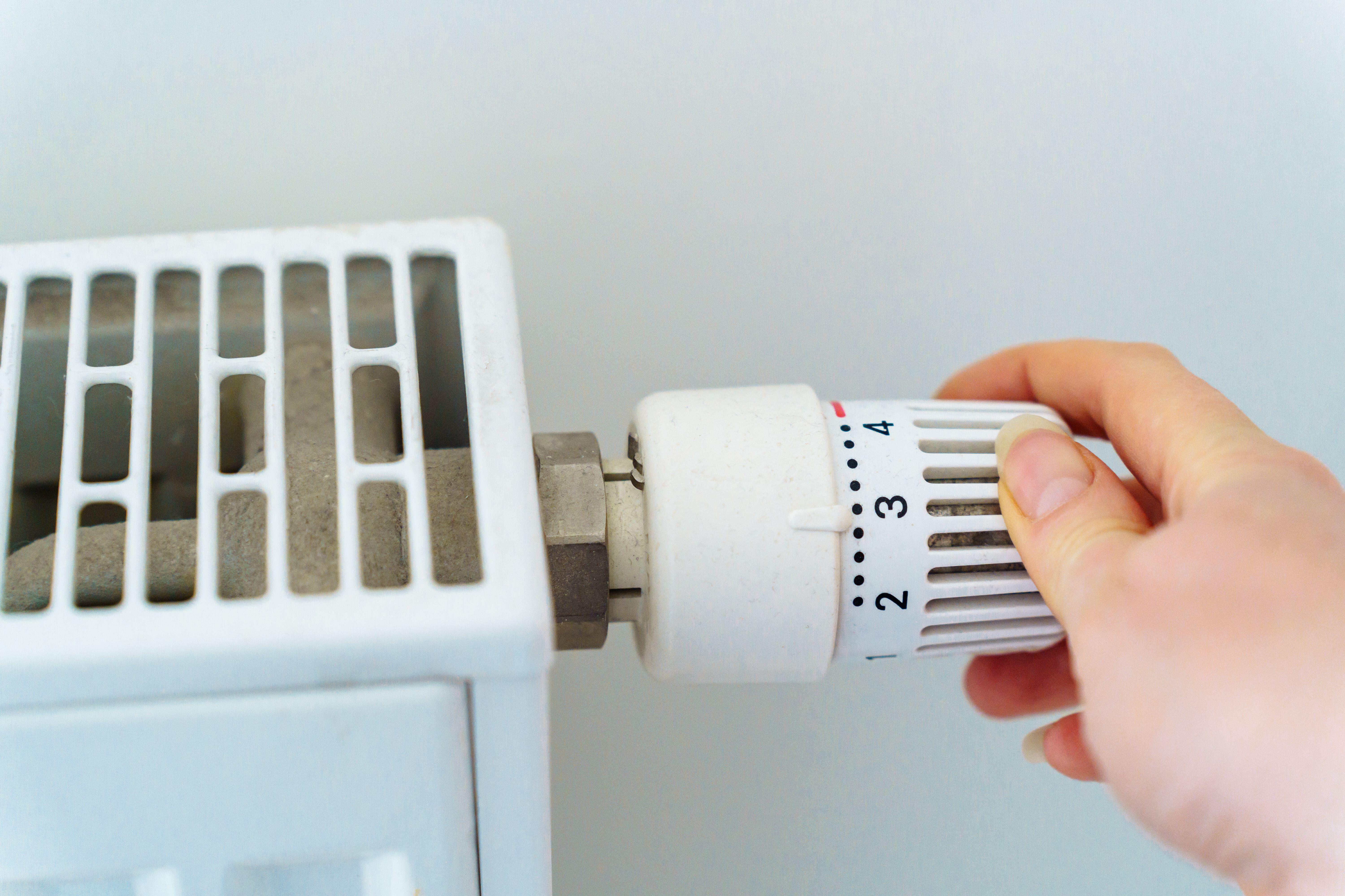 A hand turning on the regulator on the heating radiator of the house