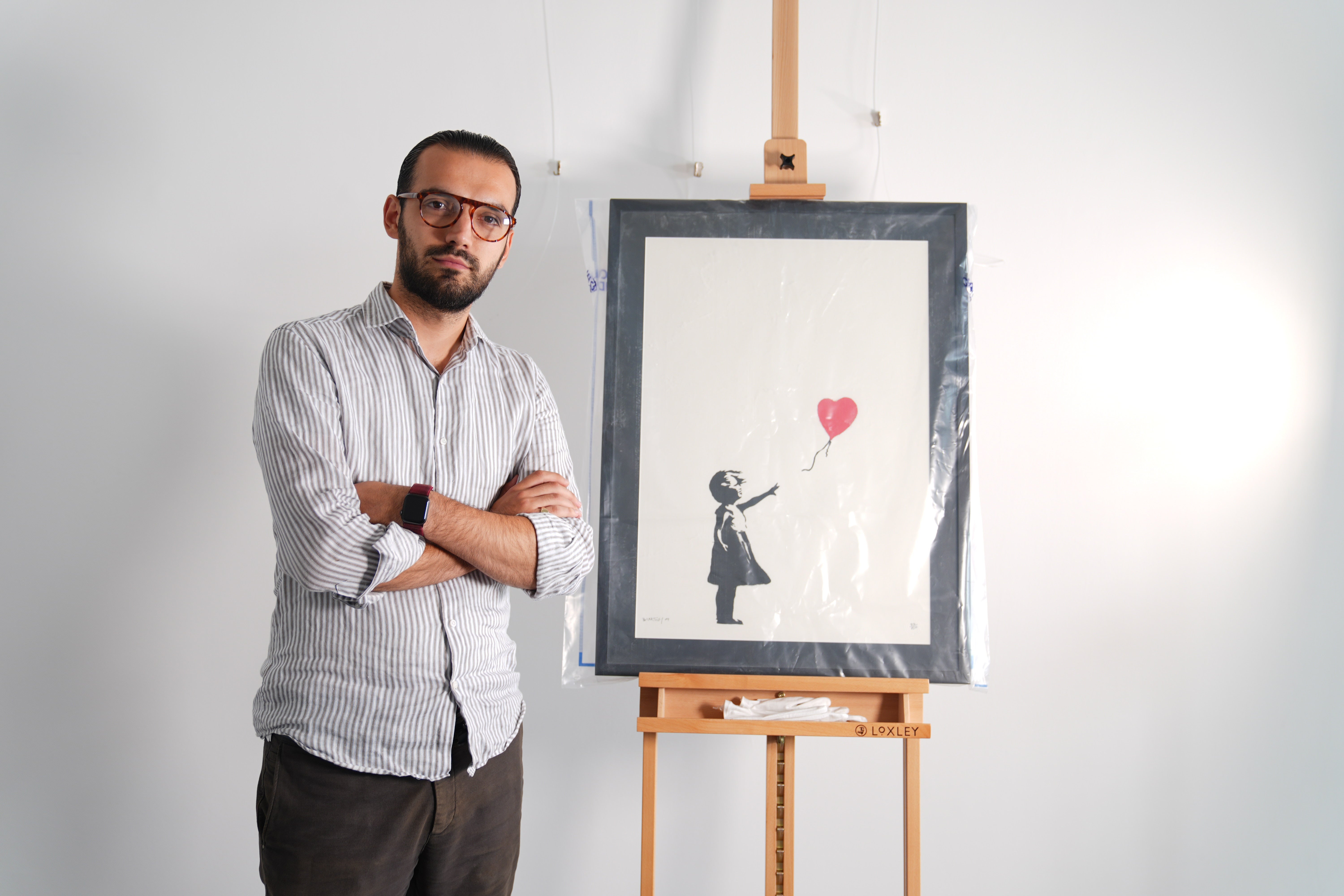 Gallery manager Lindor Mehmetaj stands with a Banksy painting