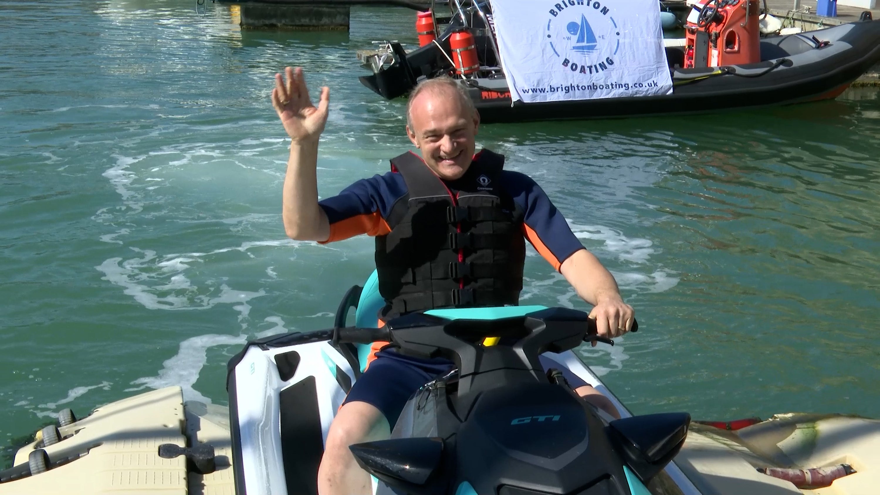 Sir Ed waving from a jet ski as he arrived in Brighton