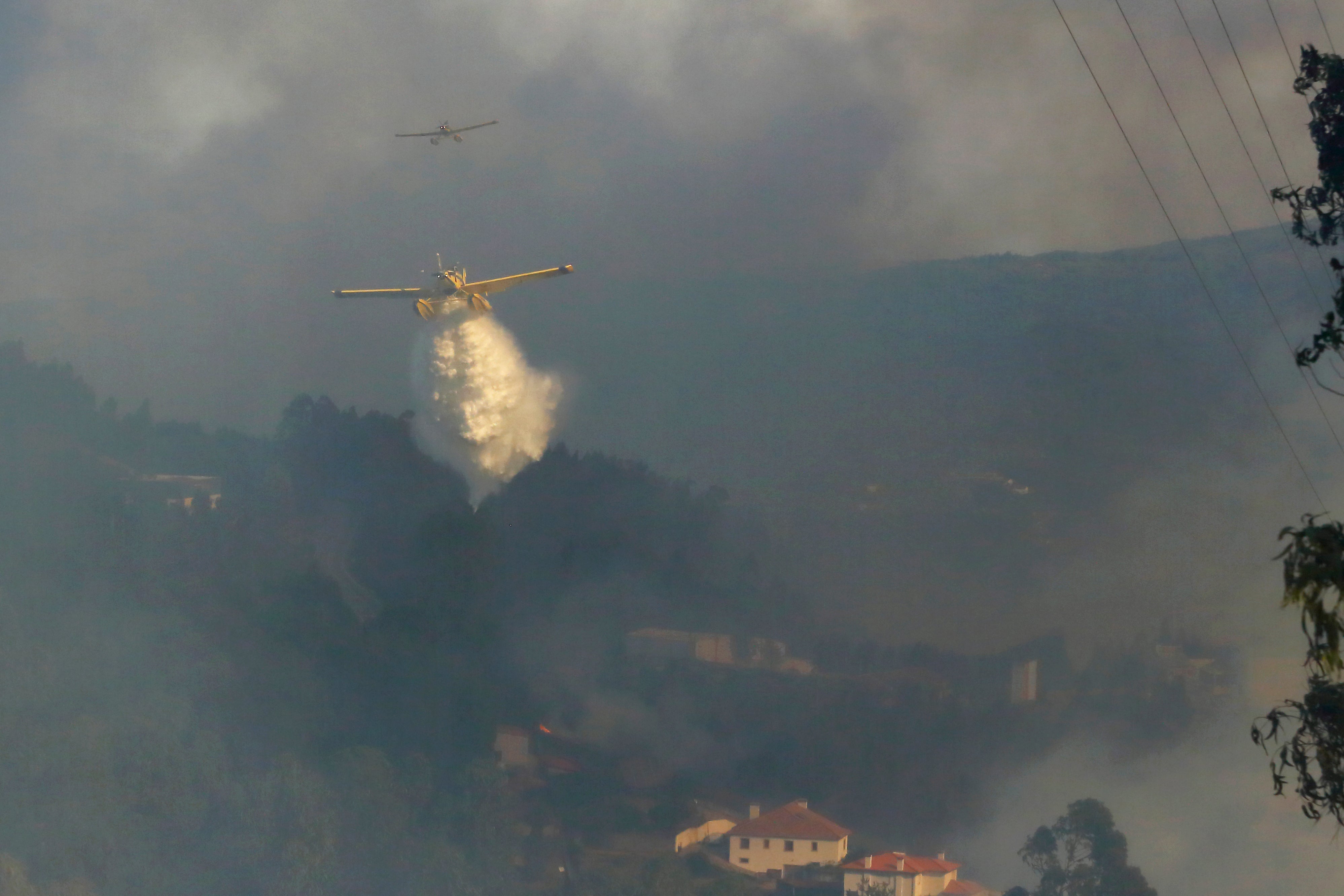 Firefighting airplanes drop water on a fire burning near houses in Sever do Vouga