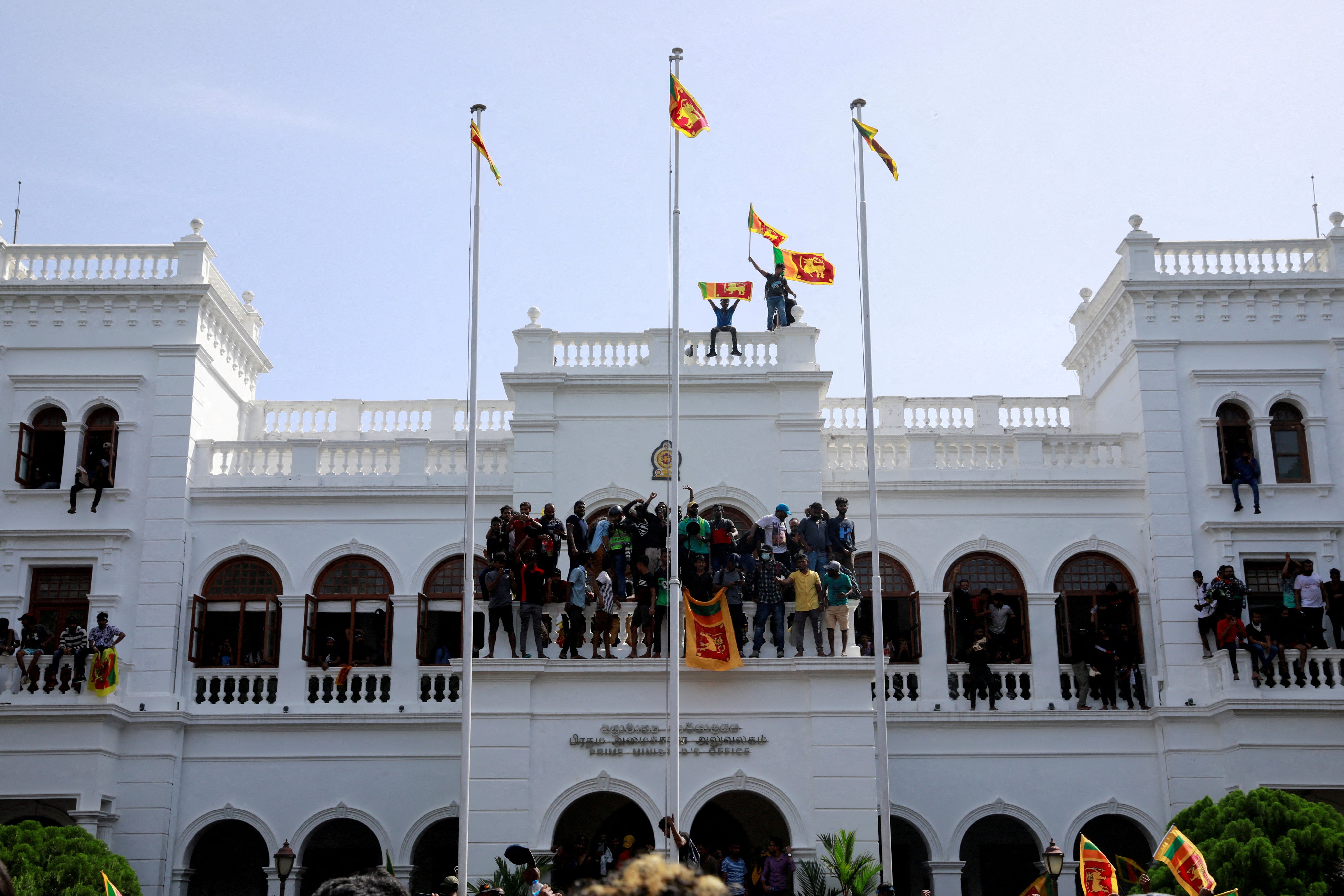 File: Protestors hold Sri Lankan flags as they stand on top of the office of Sri Lanka’s Prime Minister Ranil Wickremesinghe in July 2022