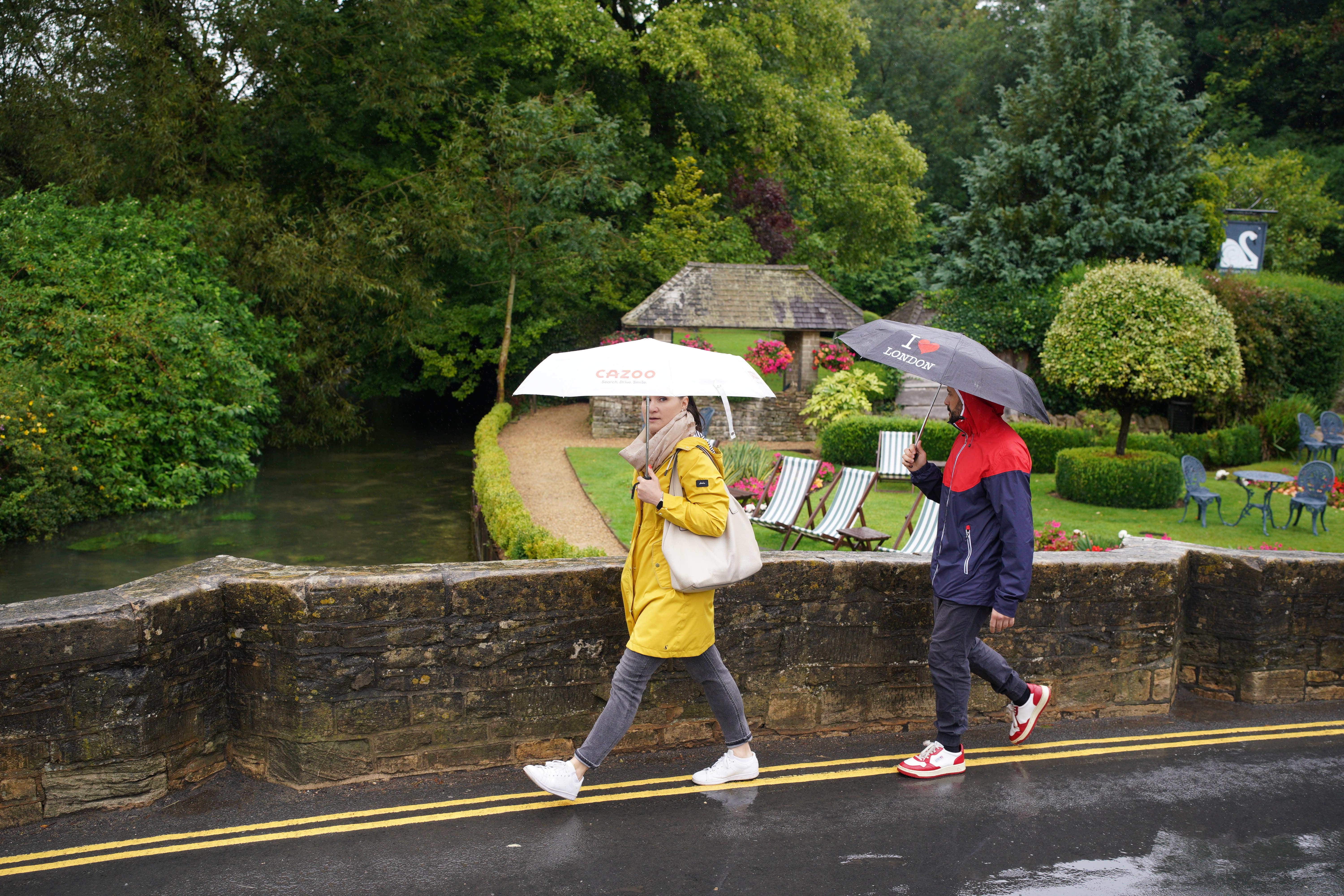 Visitors with umbrellas in the rainy weather at Bibury village in Gloucestershire (Ben Birchall/PA)