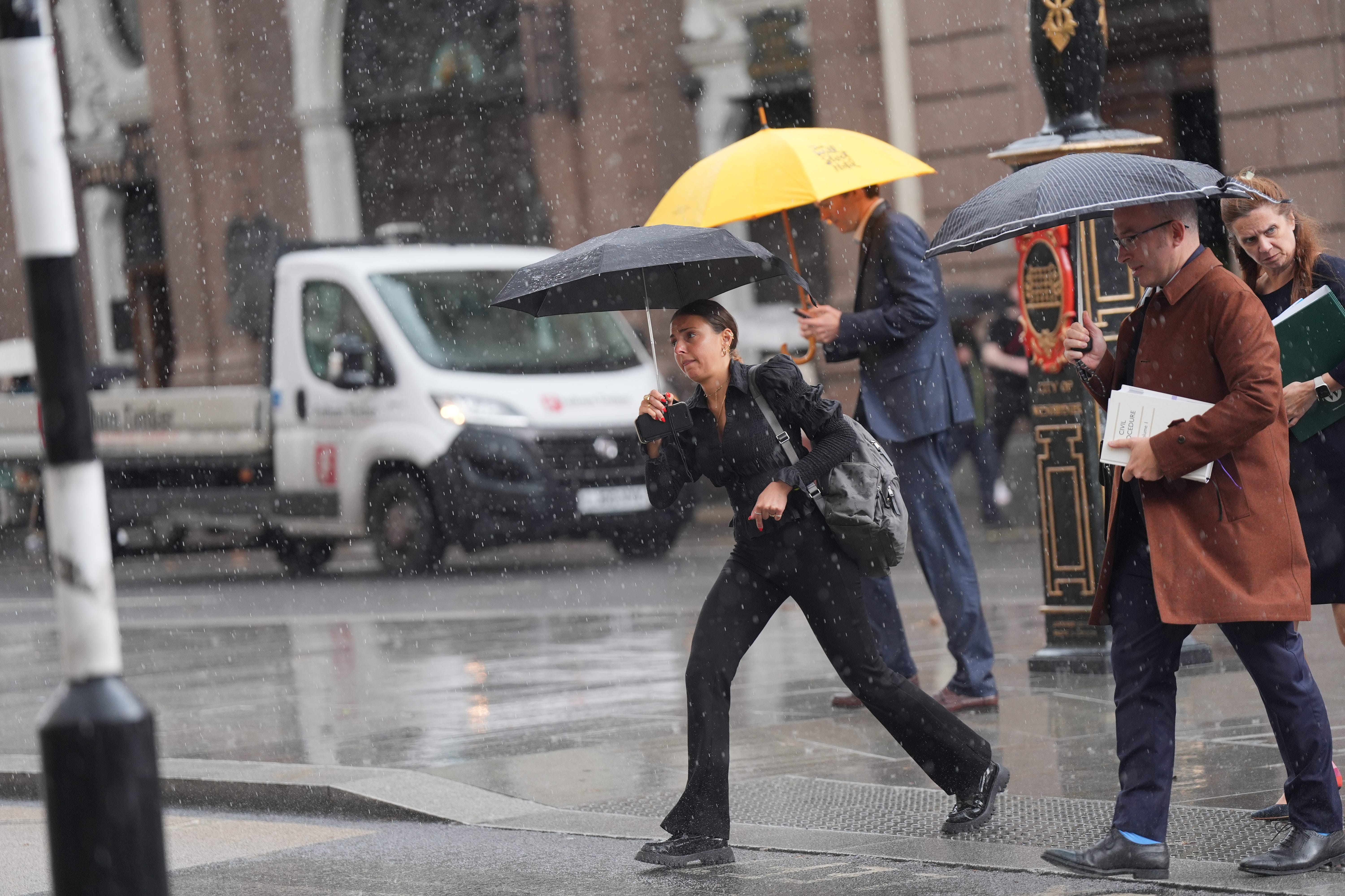 Office workers take cover beneath umbrellas during a lunchtime downpour on The Strand in central London (Yui Mok/PA)