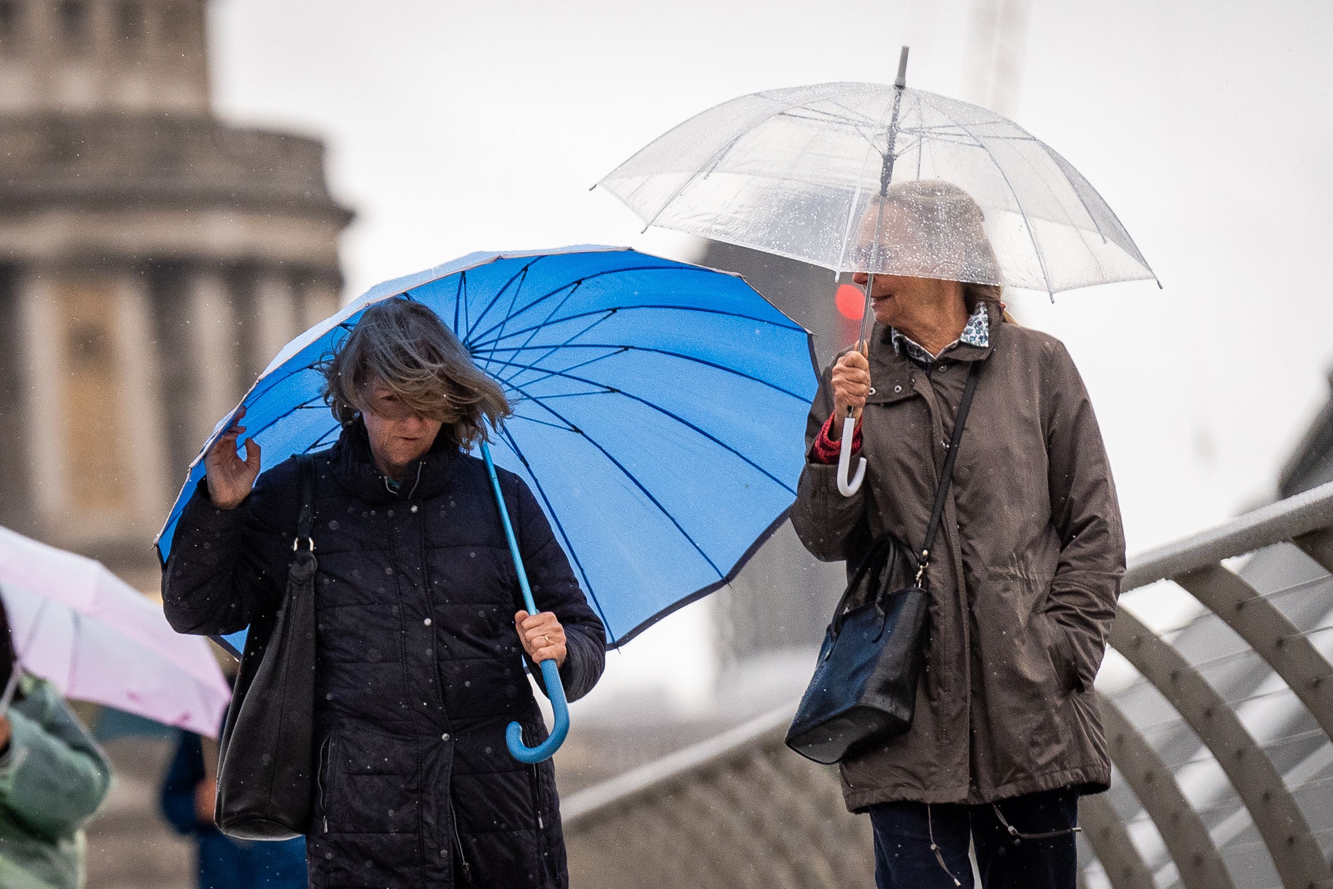 People carrying umbrellas walking through the rain on Millennium Bridge, London (Aaron Chown/PA)