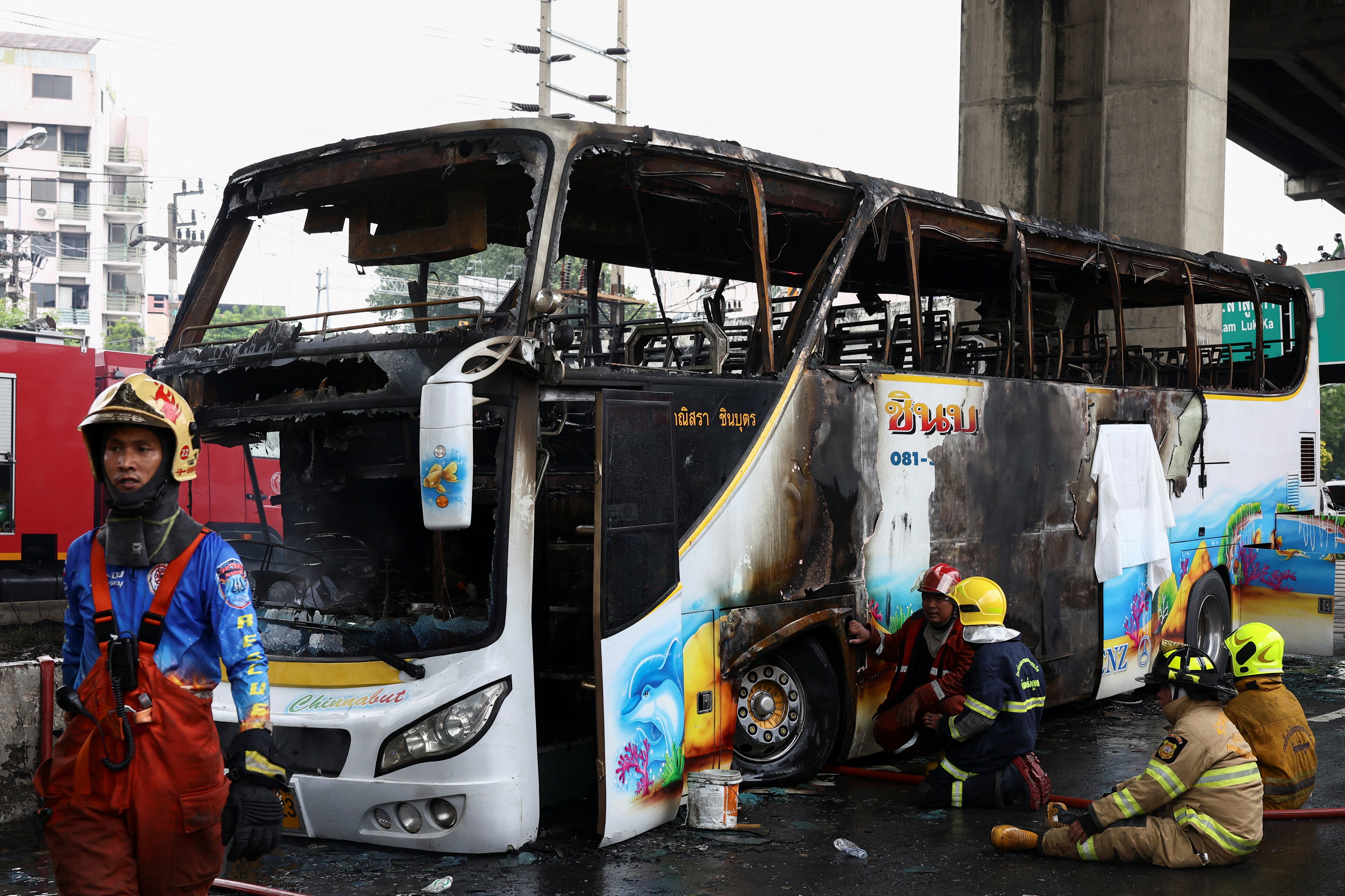 Firefighters work to extinguish a burning bus that was carrying teachers and students from Wat Khao Phraya school