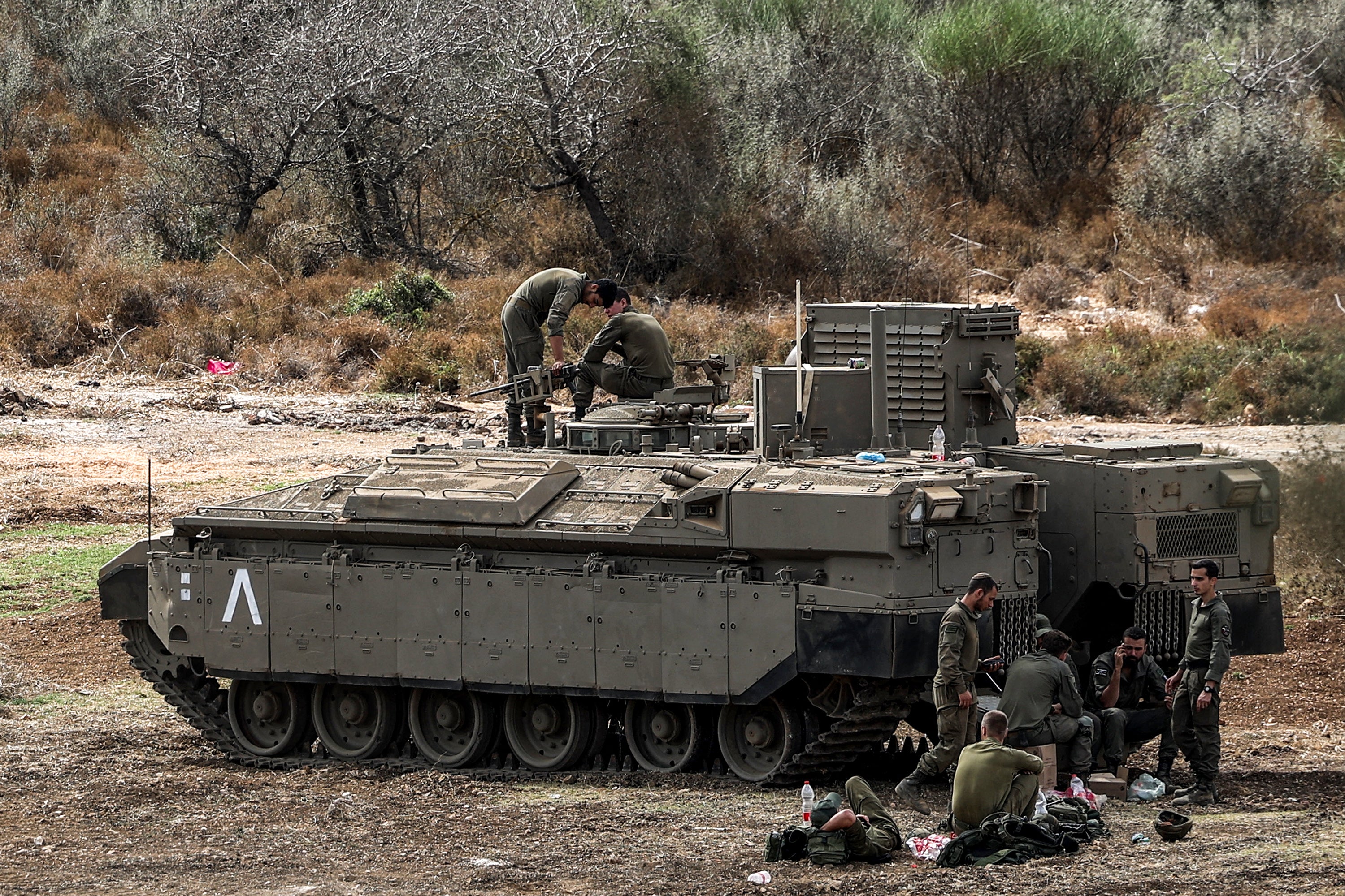 Israeli army soldiers sit by a deployed infantry-fighting vehicle (IFV) at a position along the border with Lebanon in northern Israel