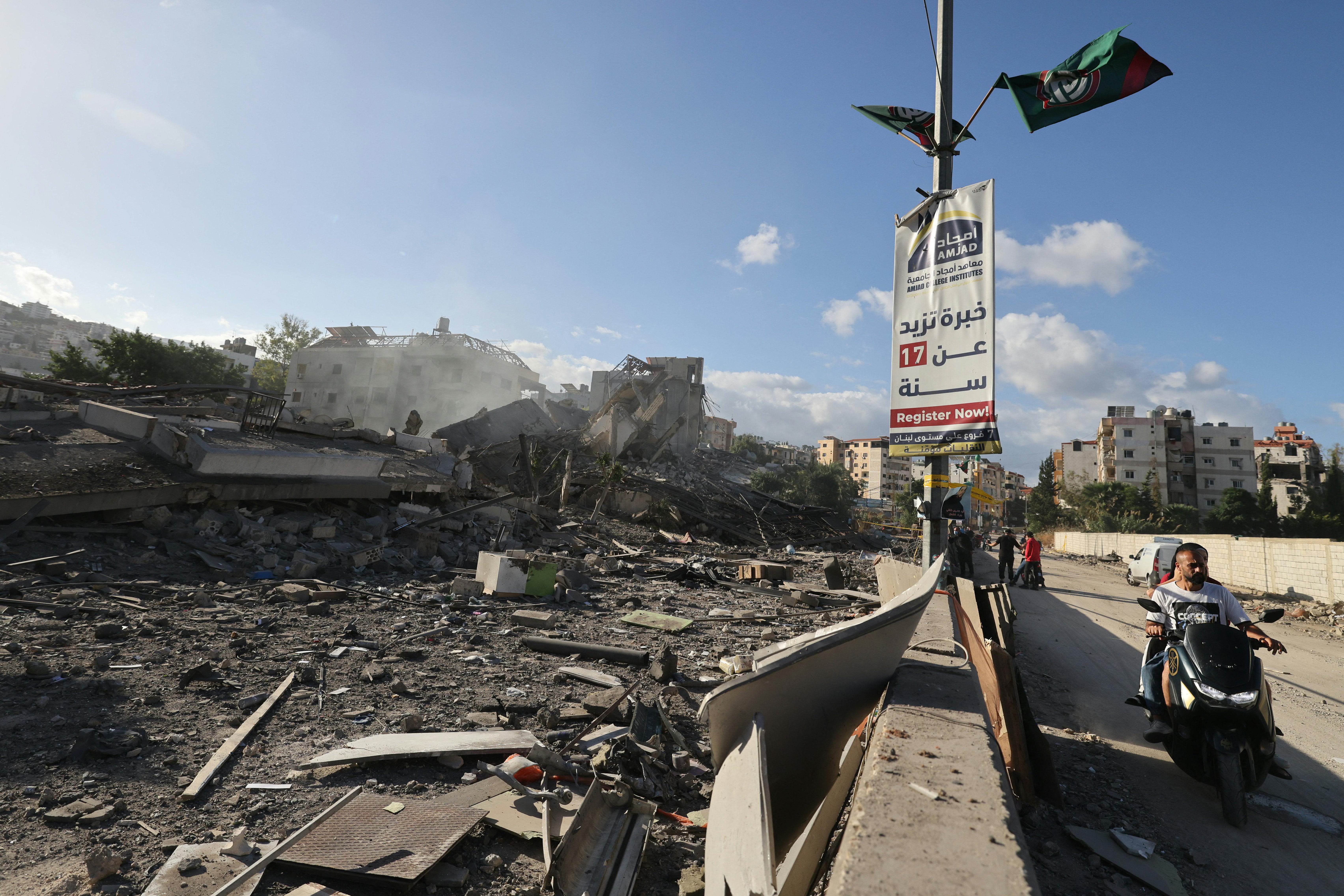 People drive past destruction at the site of an overnight Israeli airstrike in Beirut's southern suburb Tiro neighbourhood