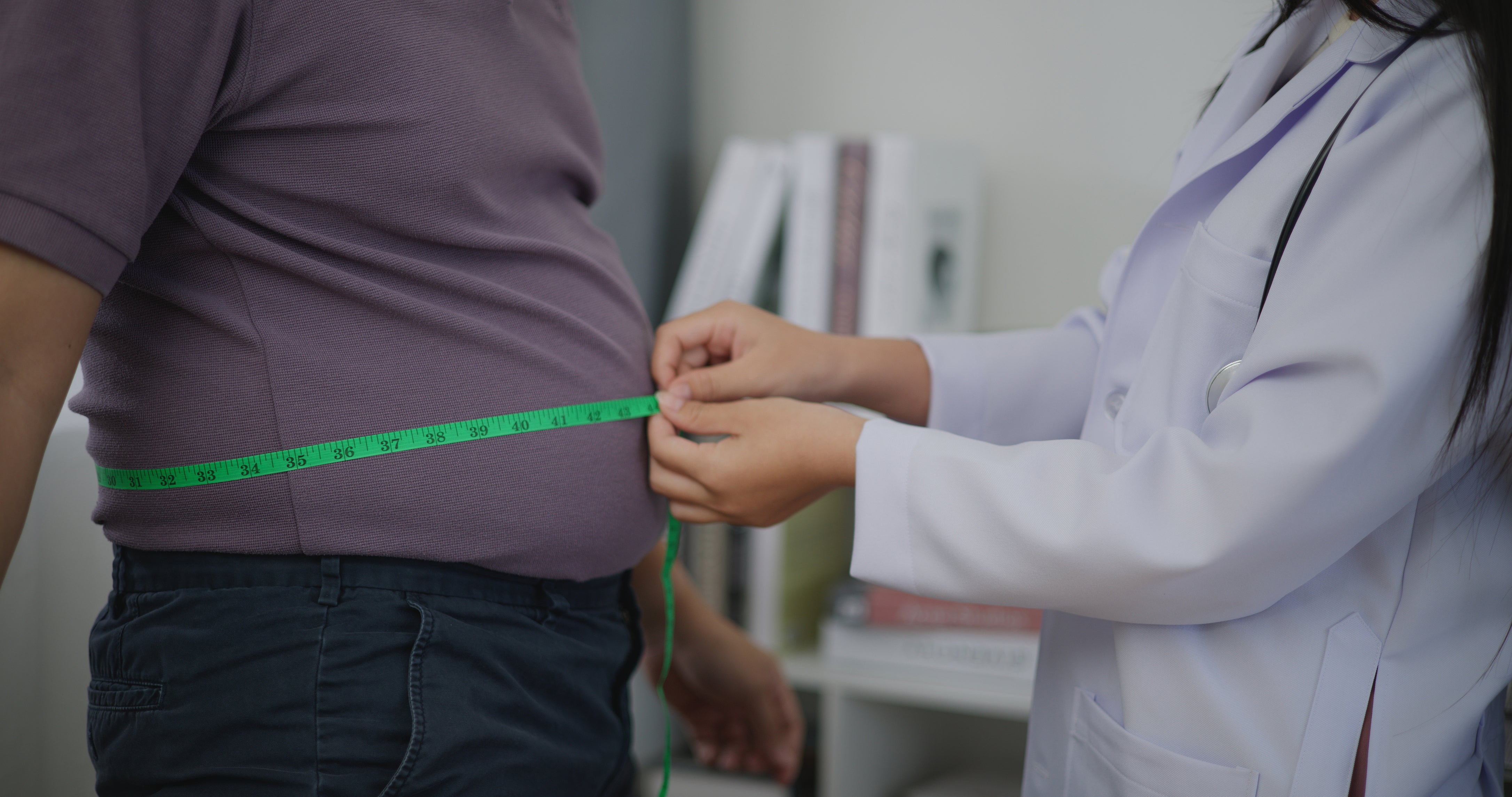 A female nutritionist measures the waist of an overweight man. Physicians project, with rising rate of obesity and other factors, U.S. life expectancy will stall by 2050