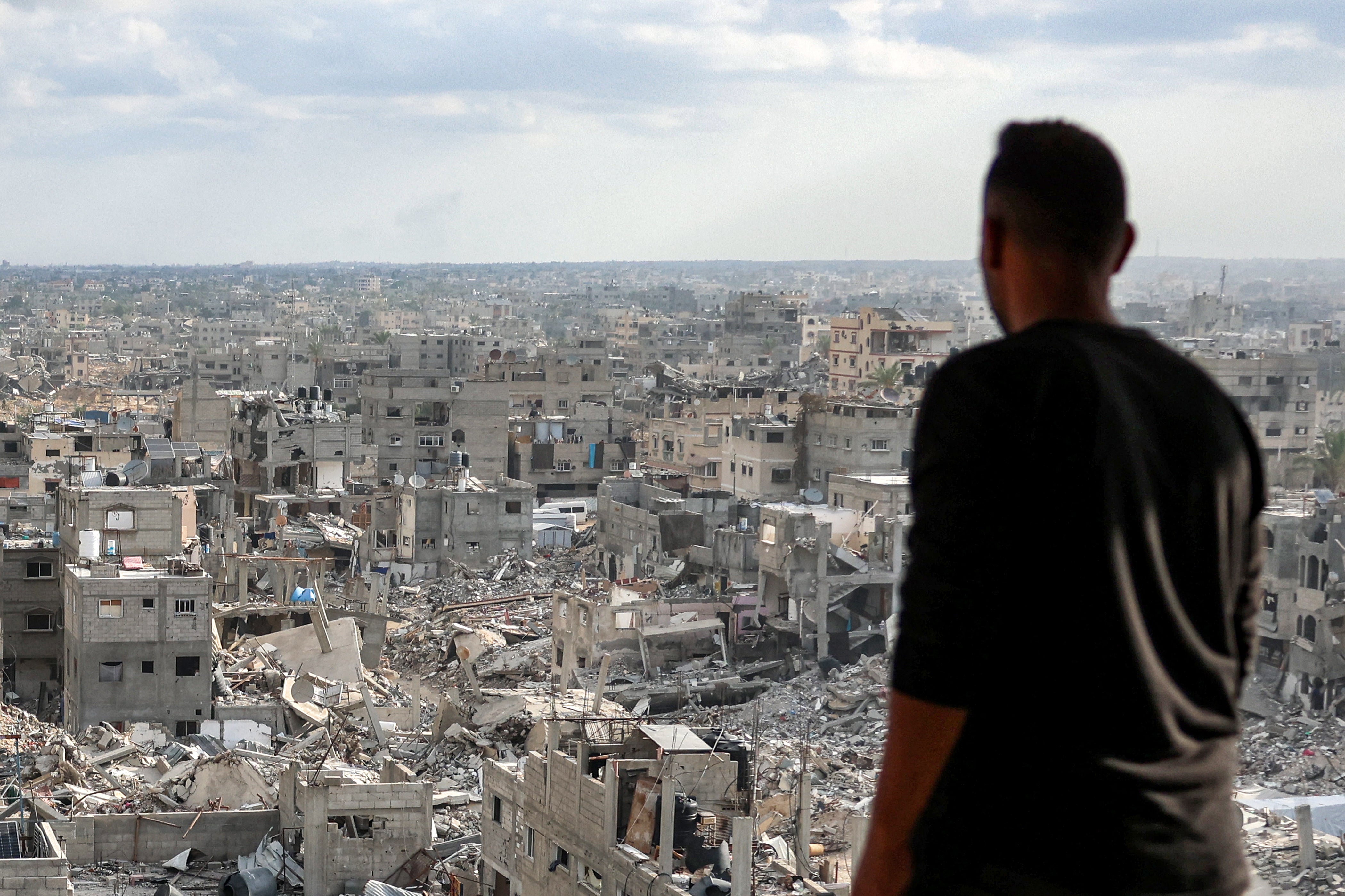 A man standing atop a heavily damaged building views other destroyed buildings in Khan Yunis in the southern Gaza Strip