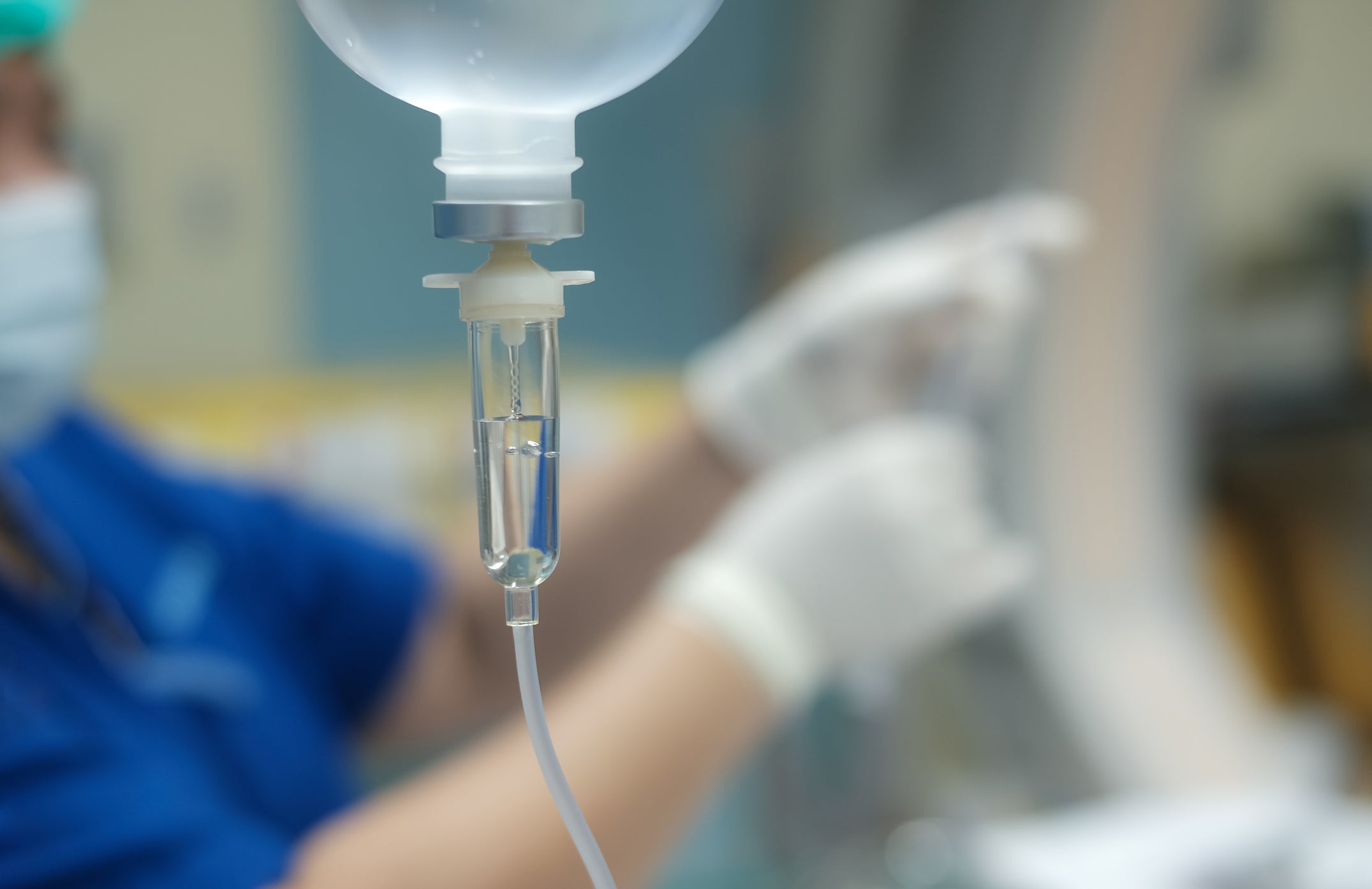 An IV line hands in front of a healthcare provider. The American Hospitals Association is calling for action from the Biden administration to respond to a nationwide shortage of the fluid, which is used to provide hydration for patients.