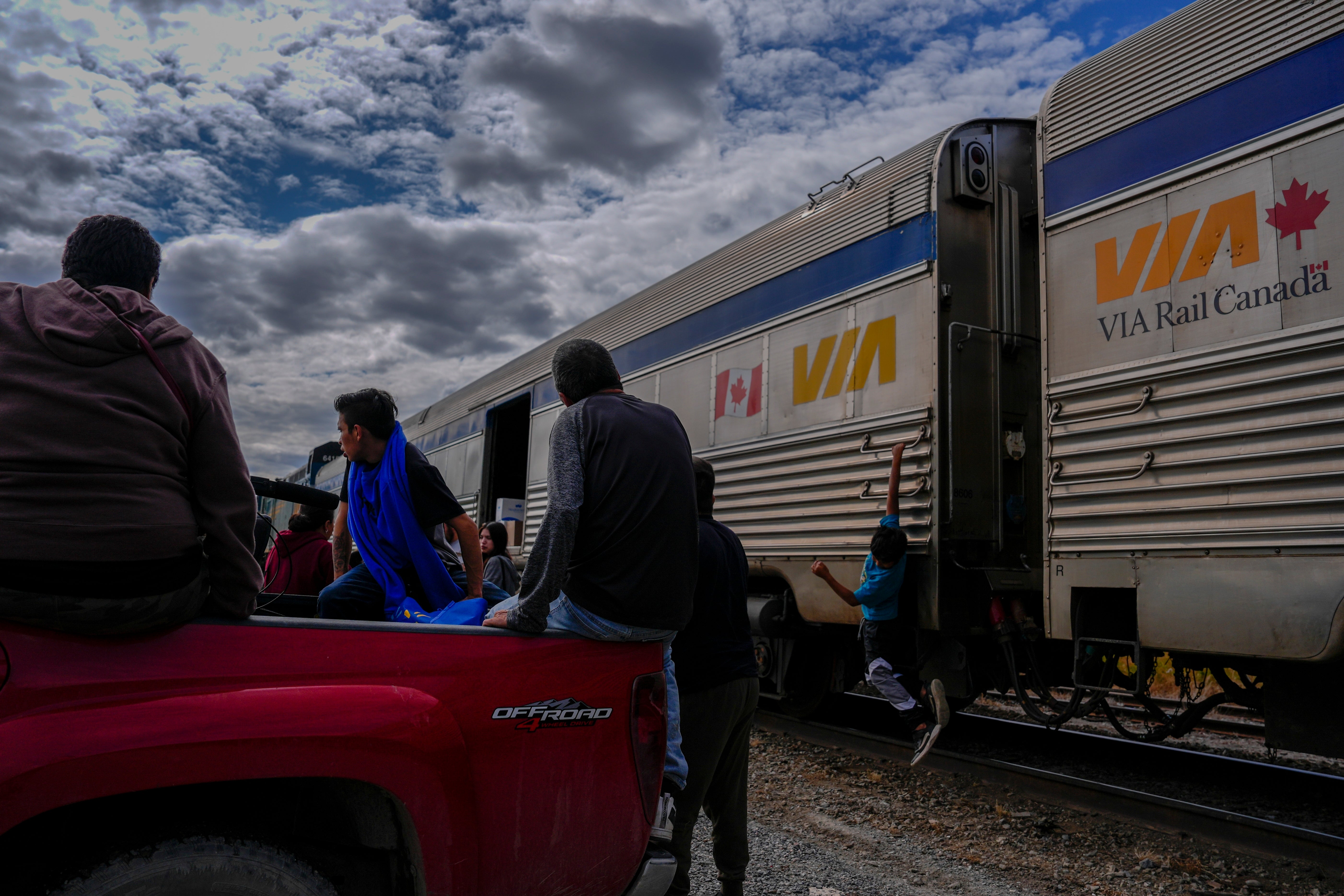 A young passenger hangs on the side of a train as others unload their belongings