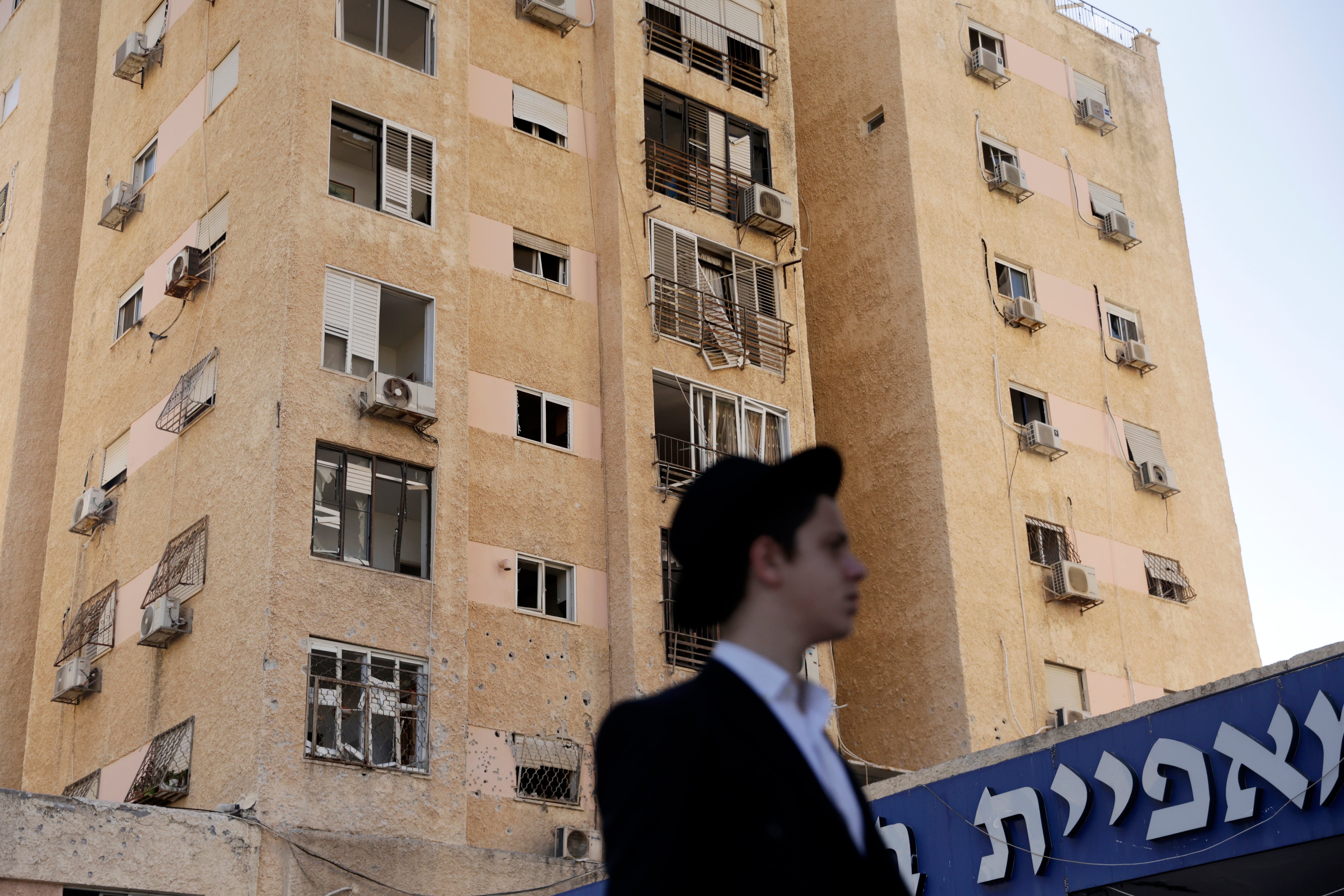 An Israeli man walks in front of a building hit by Hezbollah rocket fire on Tuesday