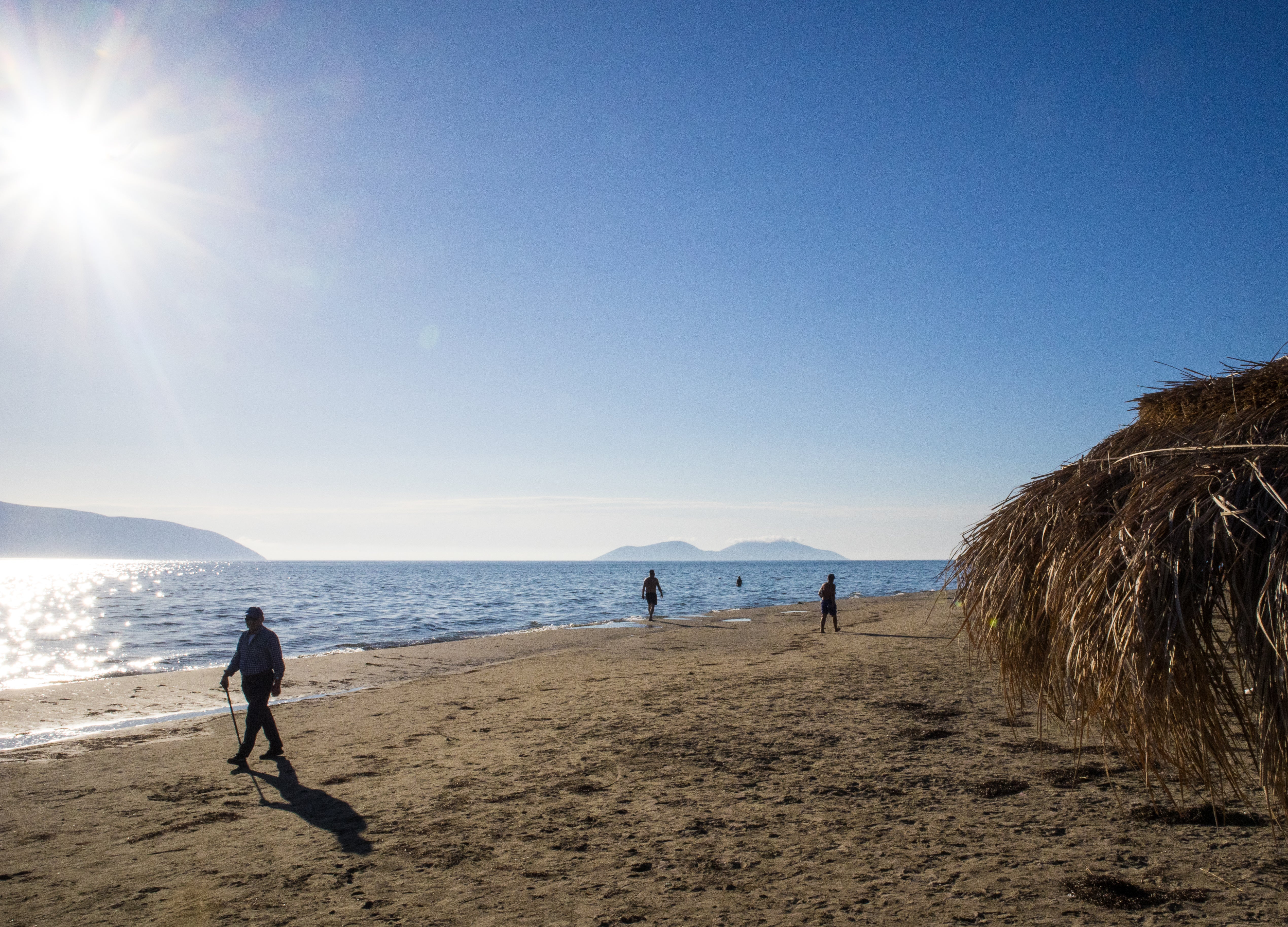 Locals walk on the beach near the region of ​​Zvernec, with Sazan island on the horizon