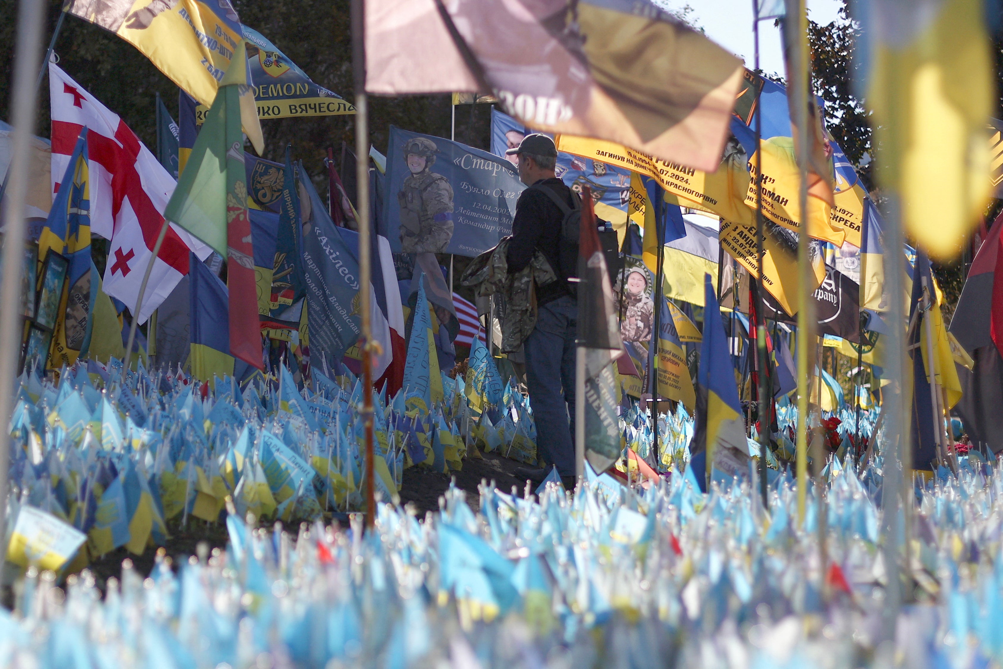 A man stands in front of a flag with the portrait of a young Ukrainian serviceman at a makeshift memorial for the fallen Ukrainian soldiers at Independence Square in Kyiv