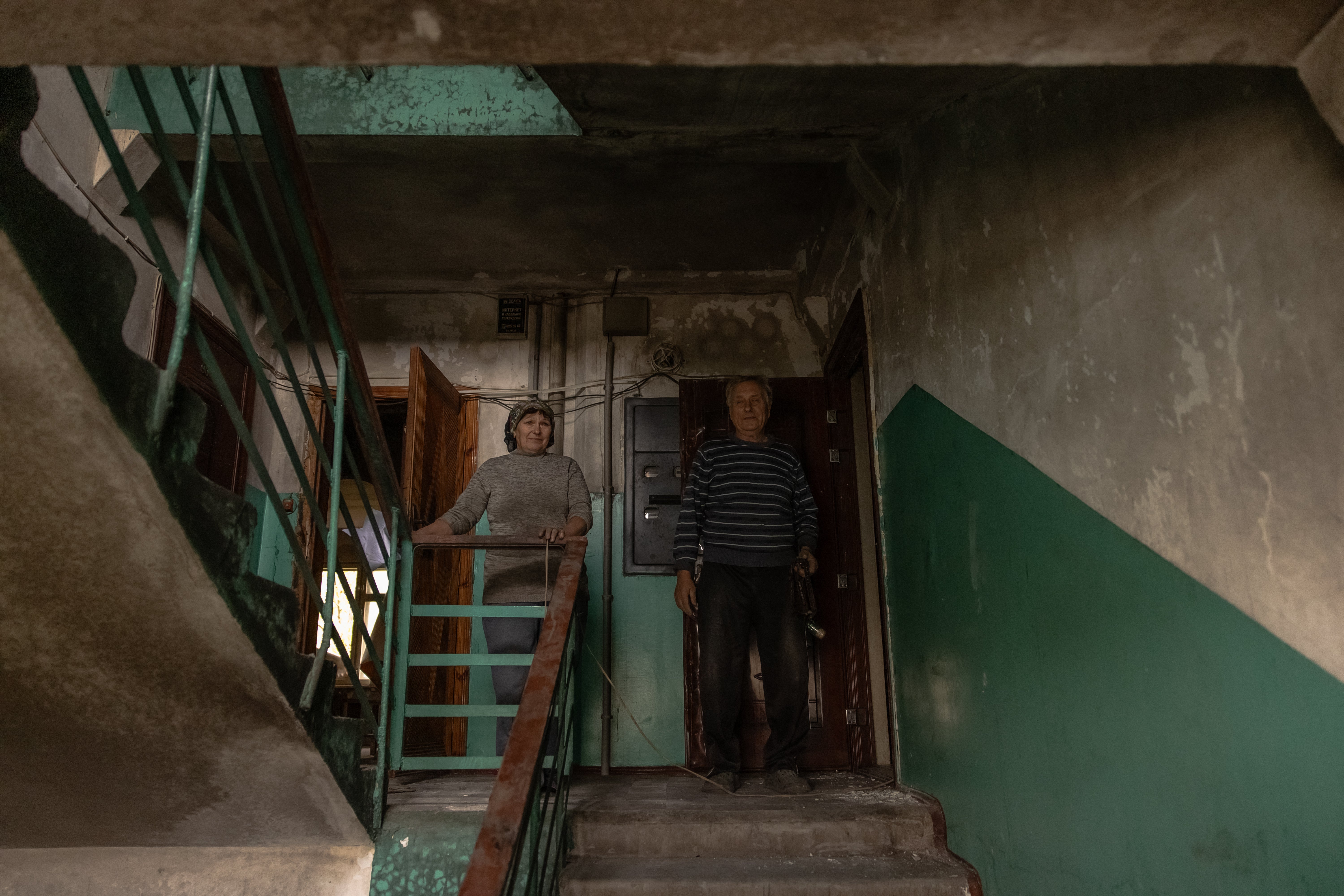 Liubov (L) and Ivan (R) Solod, 65-year-old pensioners, stand in the stairway as they visit their apartment that was recently damaged during shelling to collect their remaining belongings, in the town of Kurakhove