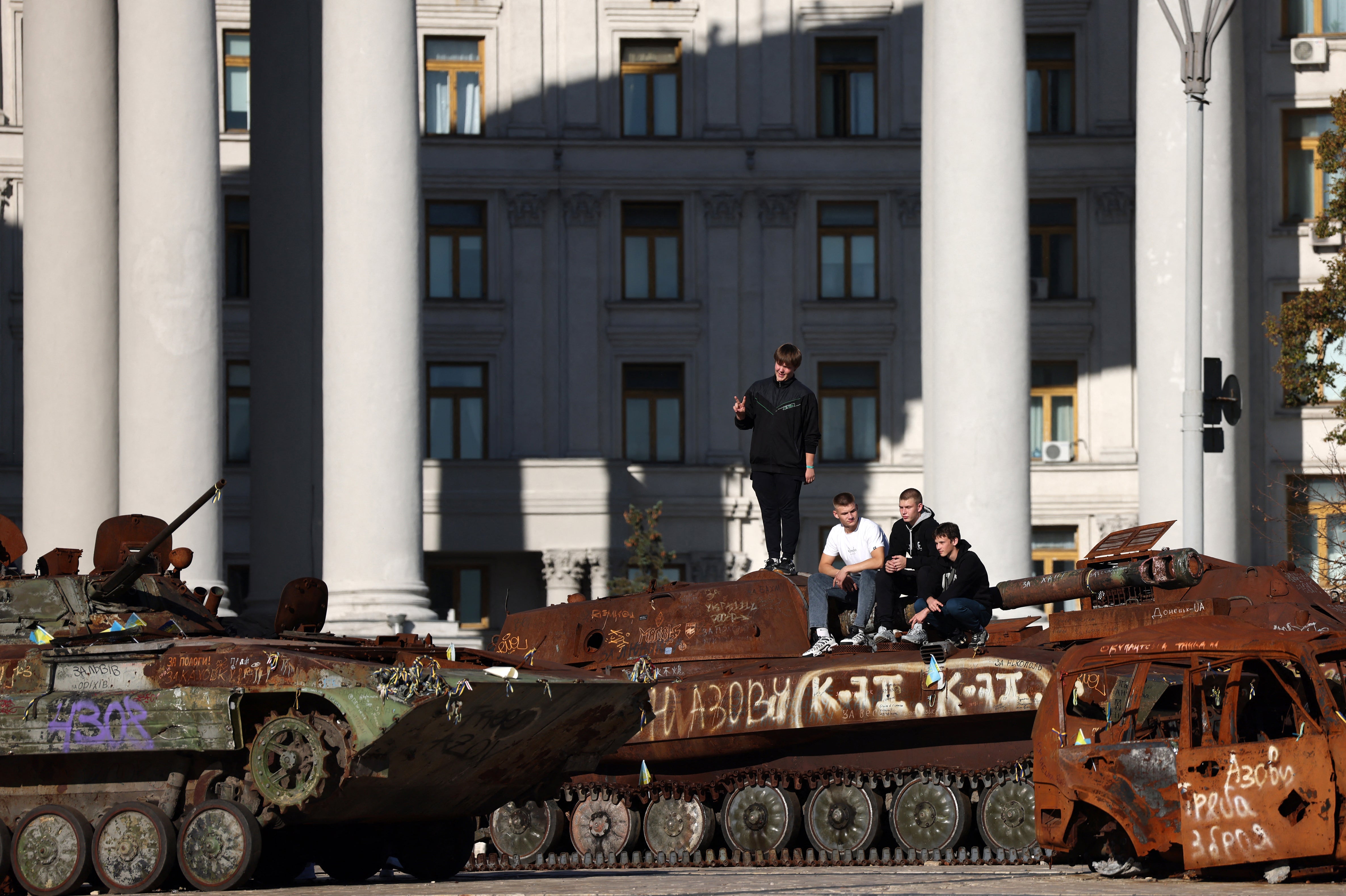 Young people sit on the ruins of Russian military equipment displayed on Mykhailivska Square in cental Kyiv