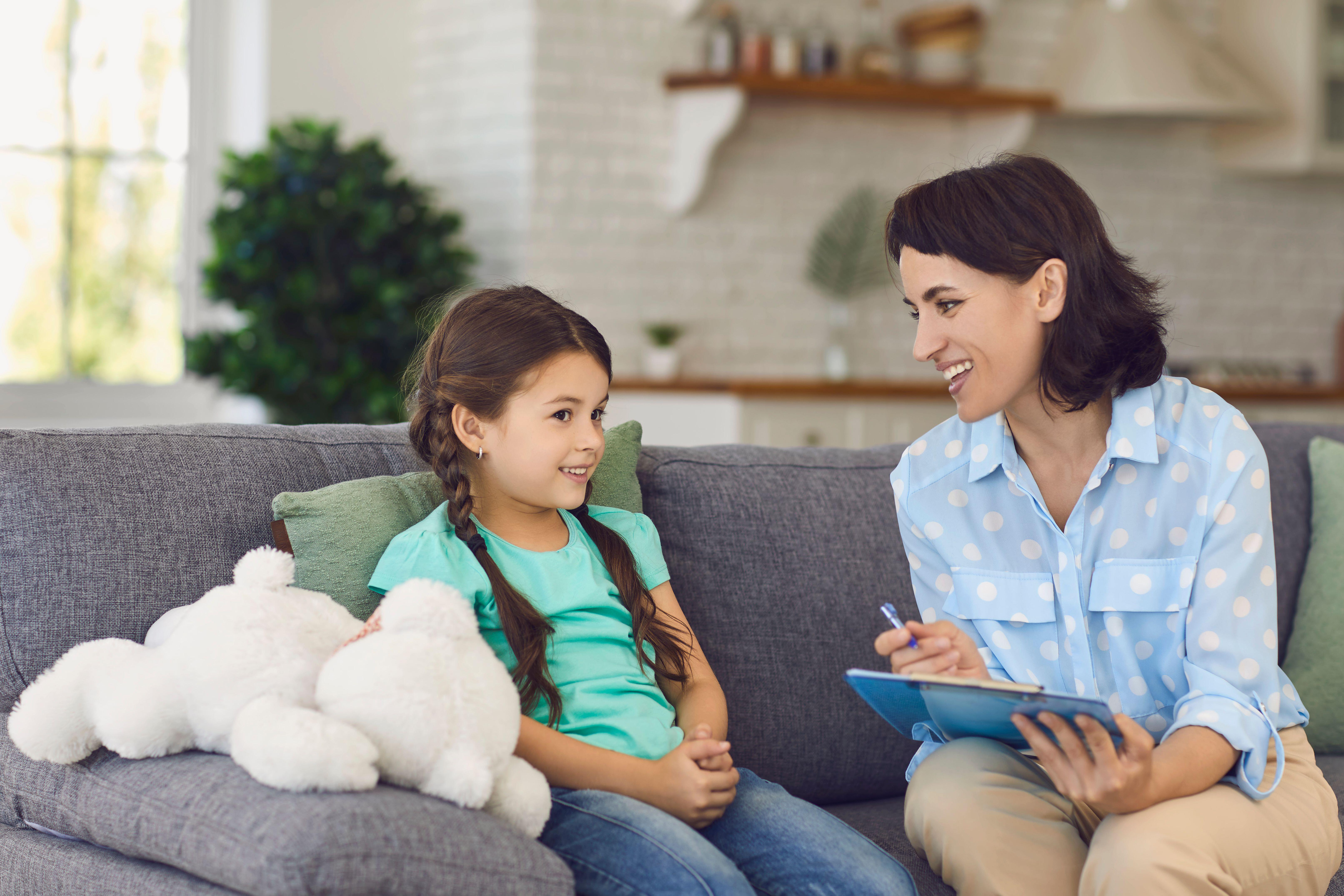 Smiling little girl talks to a cheerful child psychotherapist during a therapy session in the office