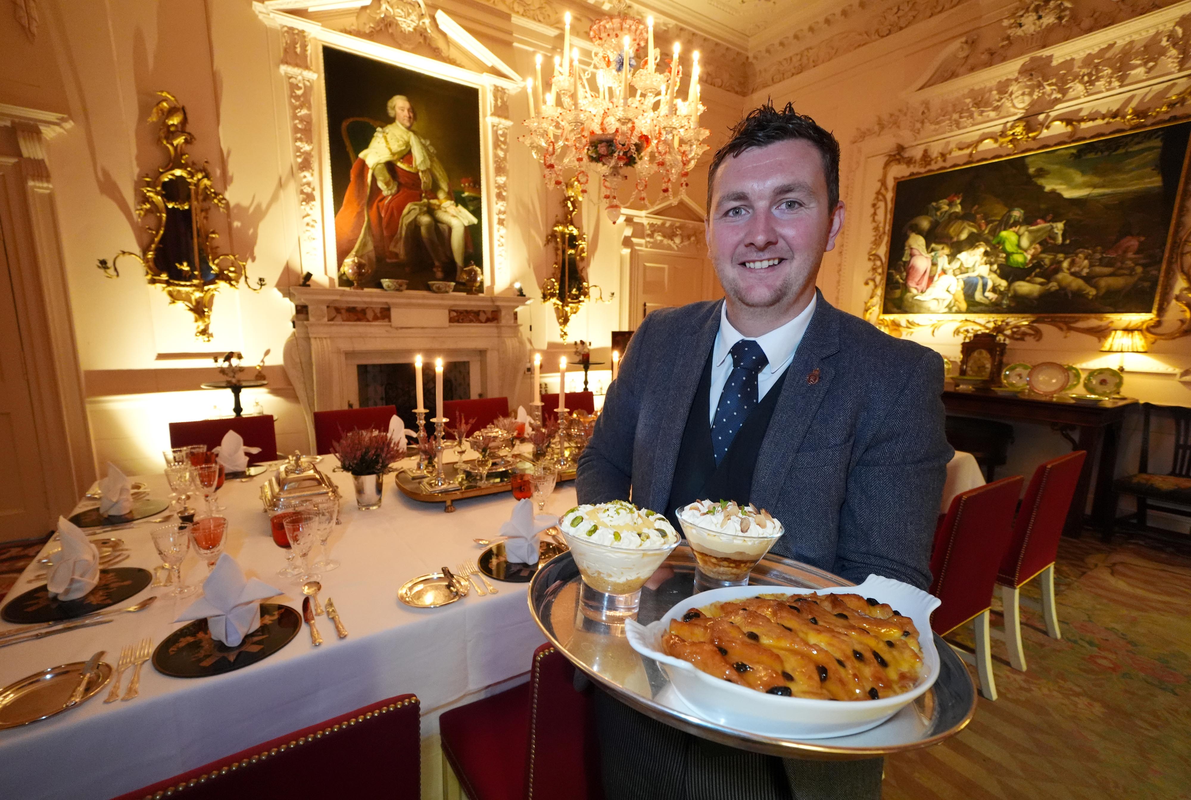 Evan Samson, who leads the front of house team at Dumfries House, with lemon and pistachio syllabub, bread and butter pudding alongside an apple and almond trifle in the Pink Dining Room (Andrew Milligan/PA)