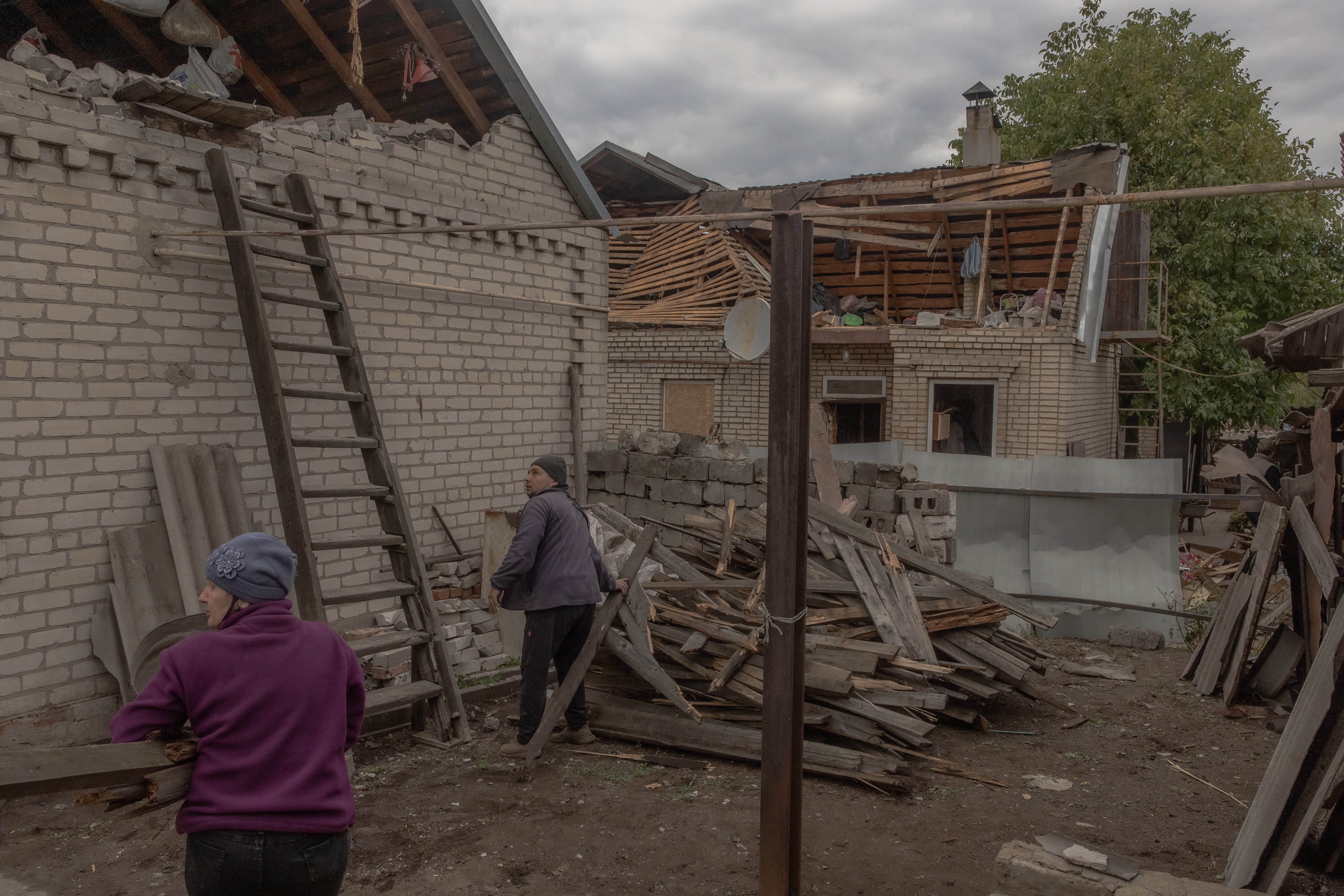 A man looks at the sky while hearing artillery explosions as he cleans debris next to a damaged house in Donetsk