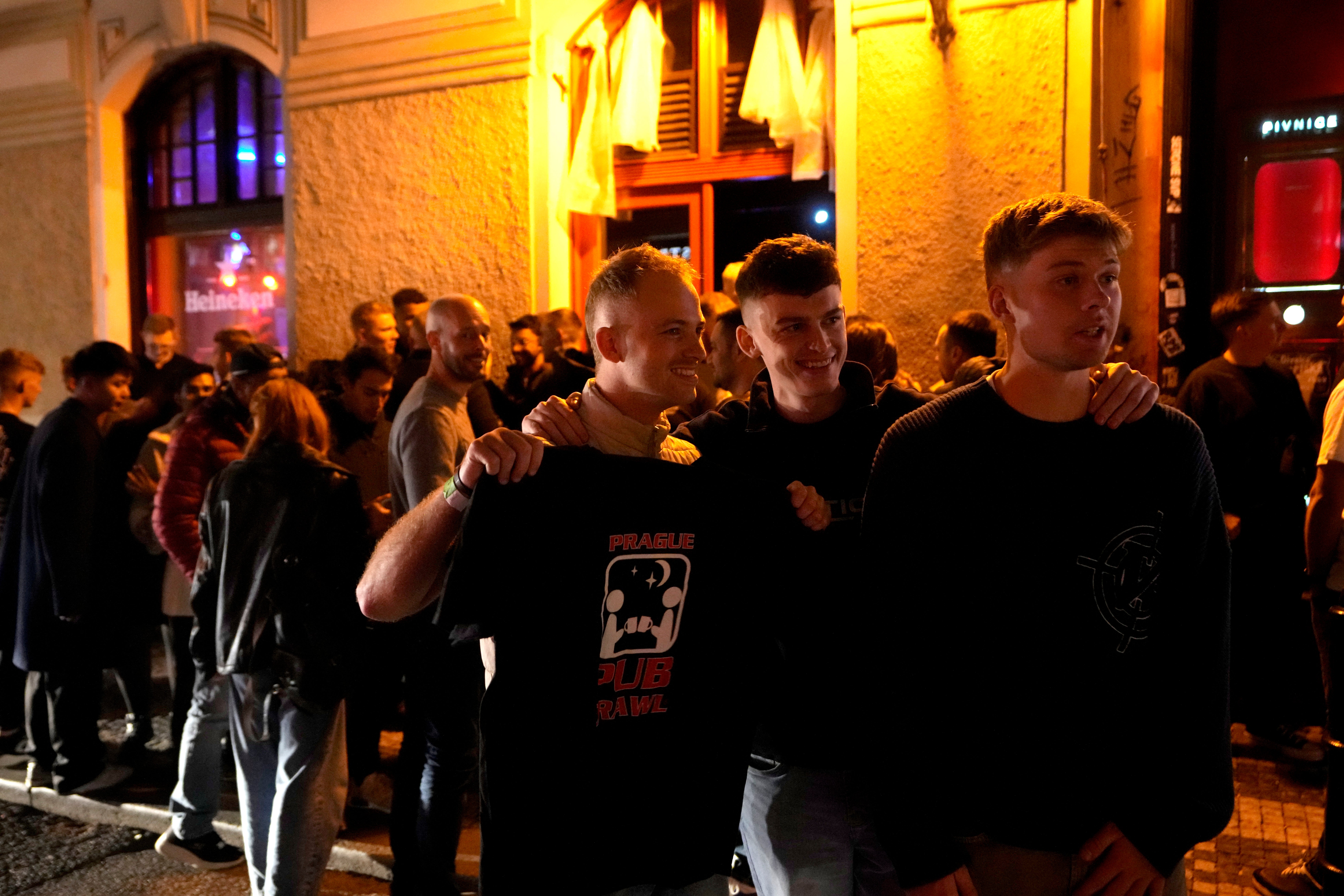 A group of tourists stand in line outside a bar as they attend a pub crawl tour in downtown Prague