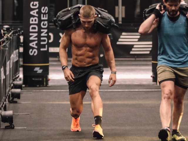<p>Hyrox UK master trainer Jake Dearden performing weighted lunges during a Hyrox race</p>